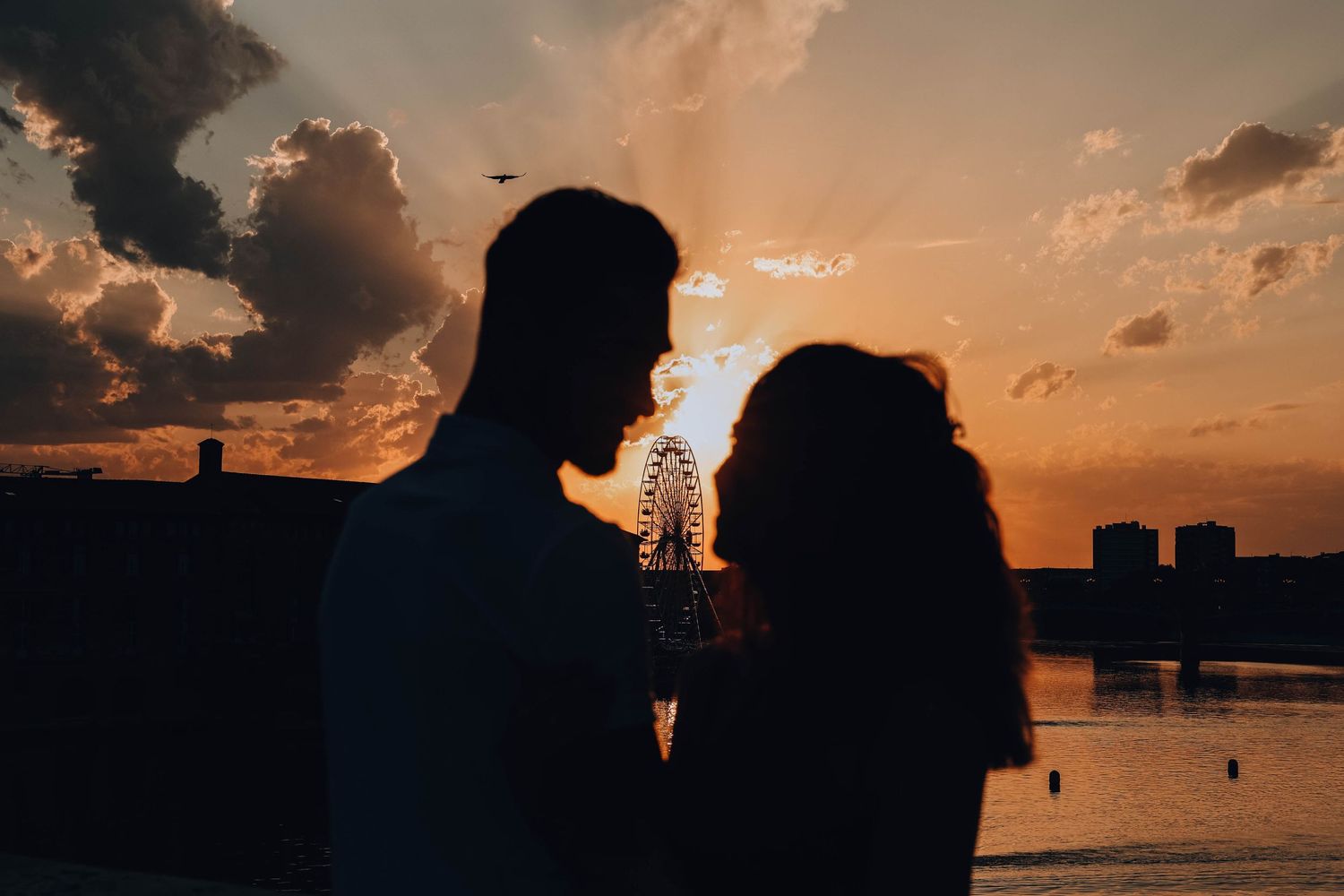 Silhouetted figures against a dramatic sunset sky over water.