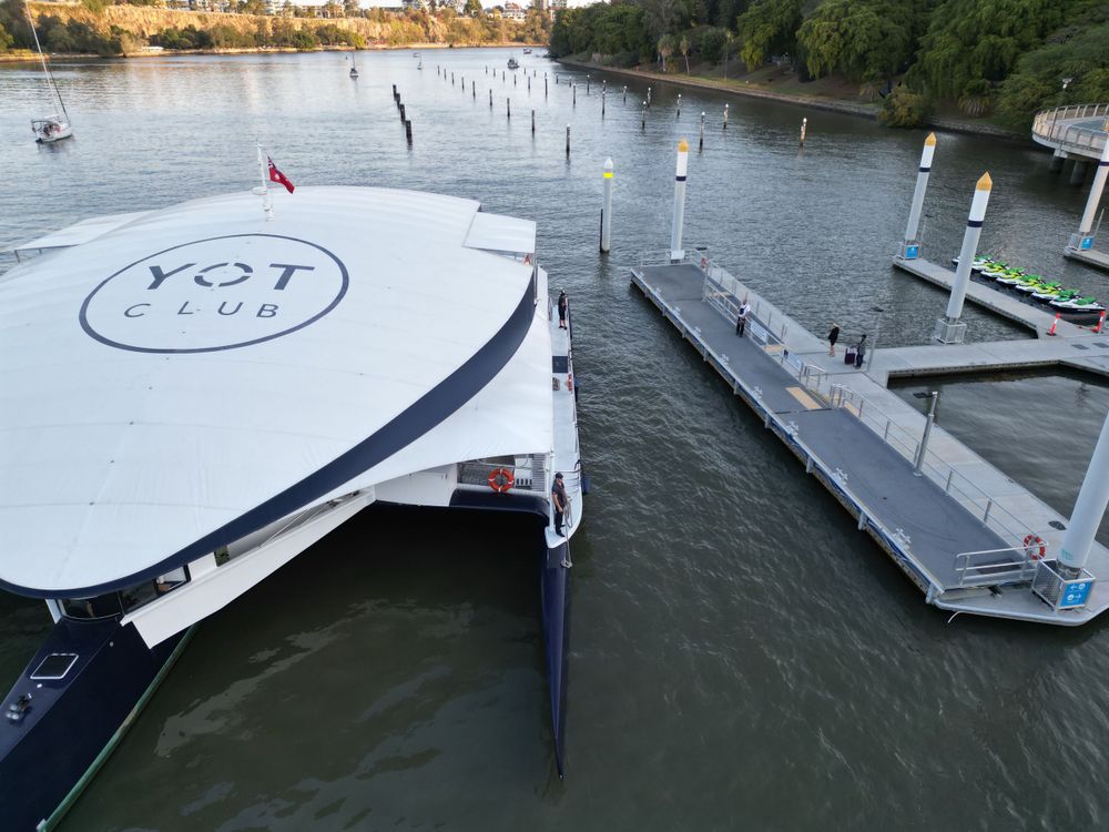Aerial view of white YOT vessel and floating dock system on river.