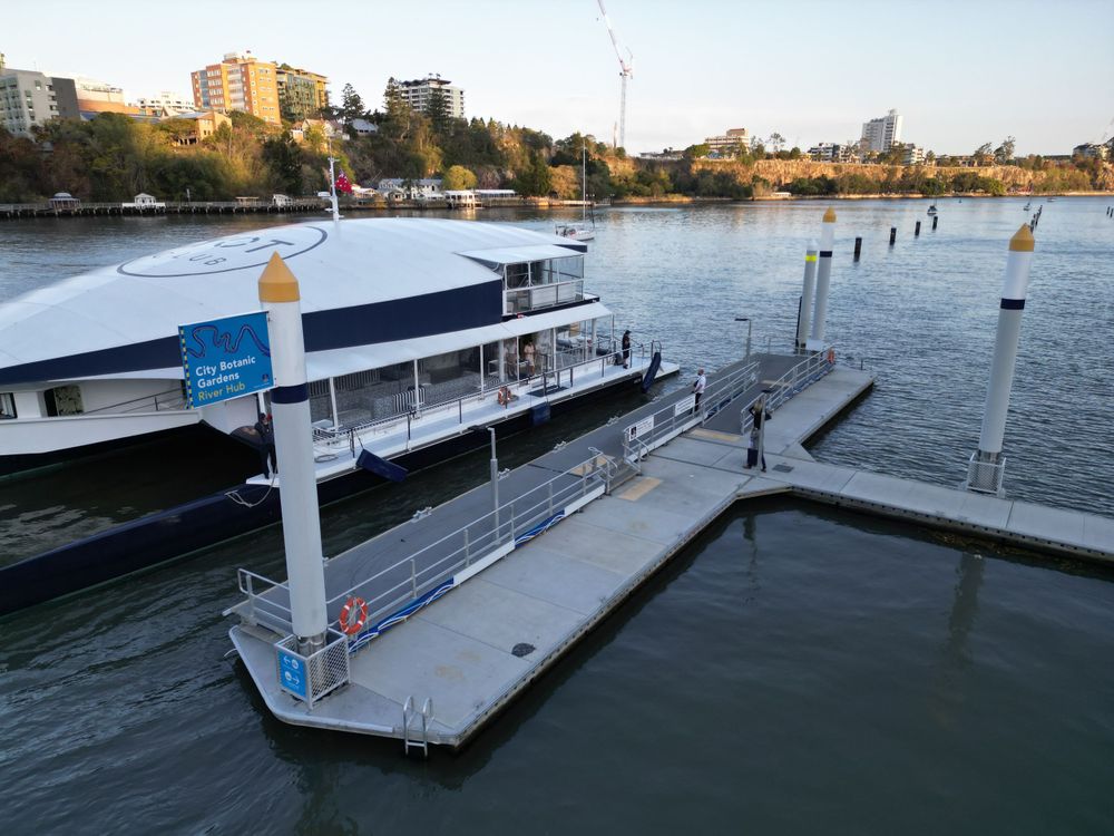 Modern ferry terminal with floating dock and passenger vessel on urban waterway.