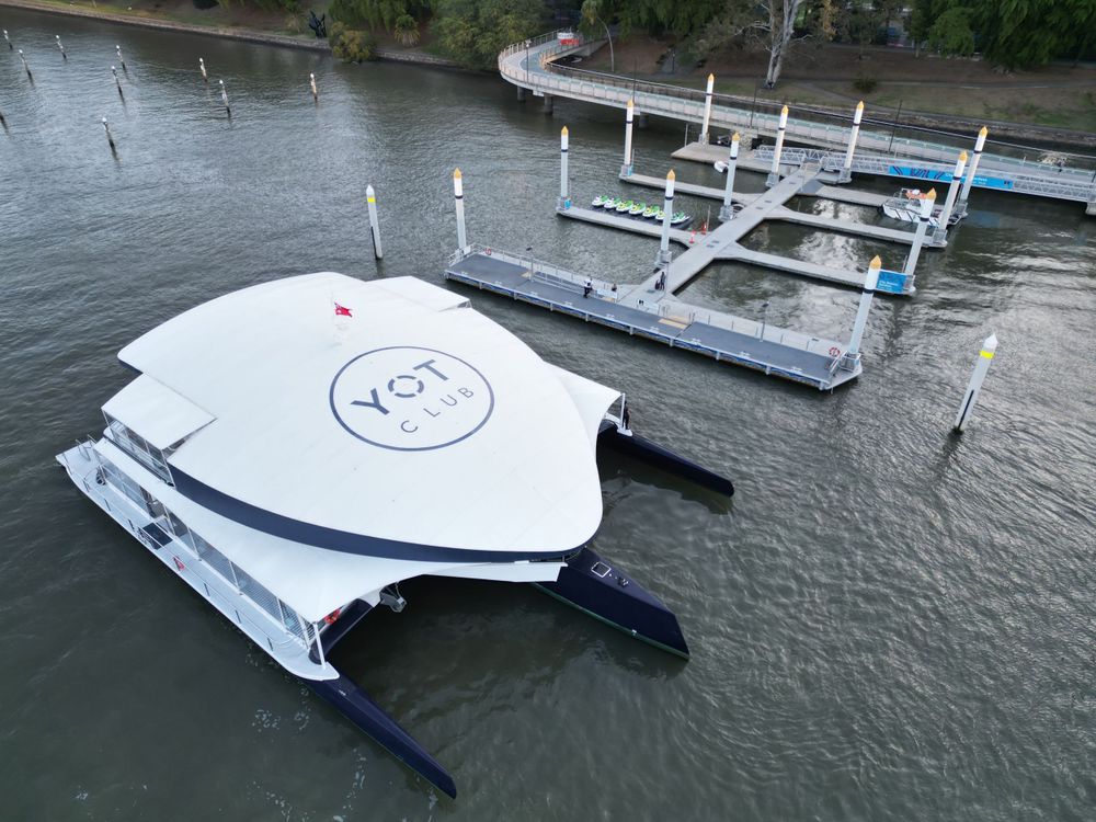 White catamaran-style vessel with 'YOT' branding moored at floating dock.
