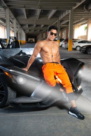 Athletic model in orange pants poses with luxury sports car in parking garage.