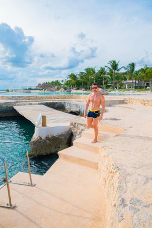 Beachgoer walking down stone steps at tropical resort waterfront.