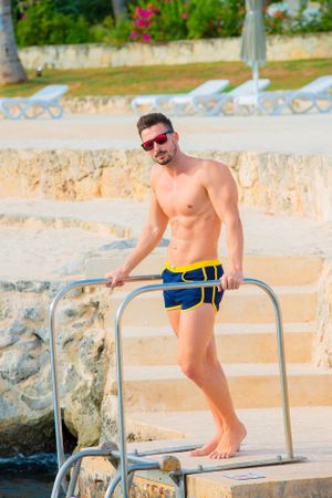 Swimmer in blue shorts poses on diving platform at resort pool.