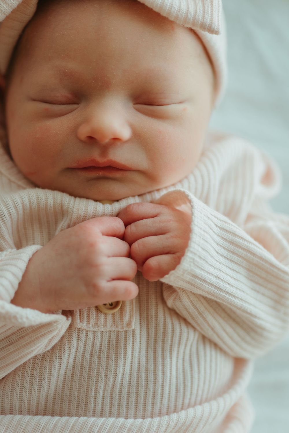 A sleeping newborn wears a cozy white knit sweater.