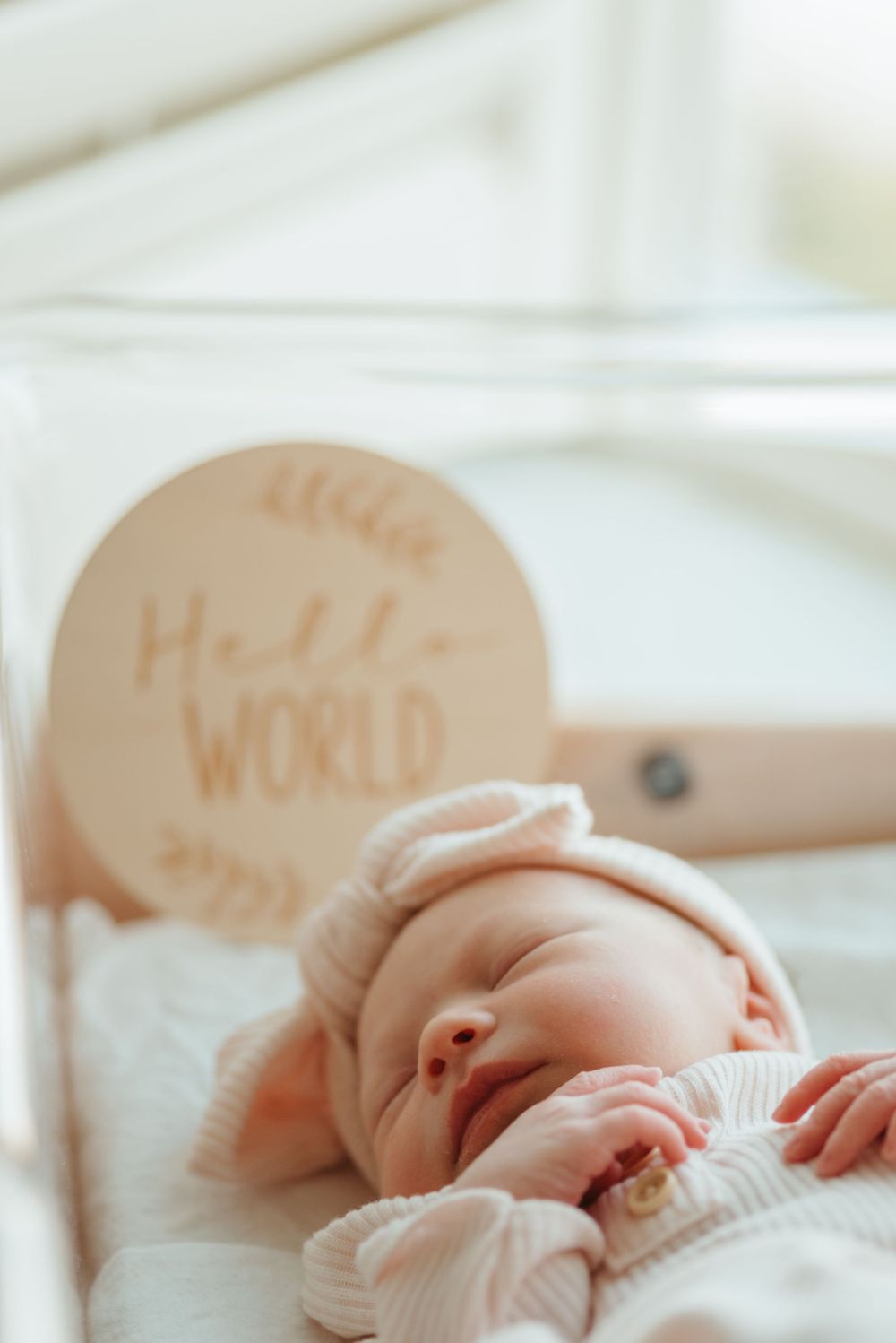 A newborn rests on white bedding with 'Hello World' wooden signs in the background.