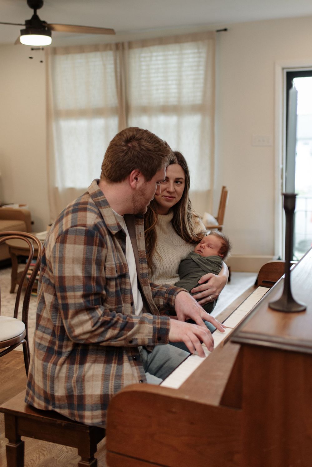 Family moment at piano as parents share music with their newborn in sunlit room.