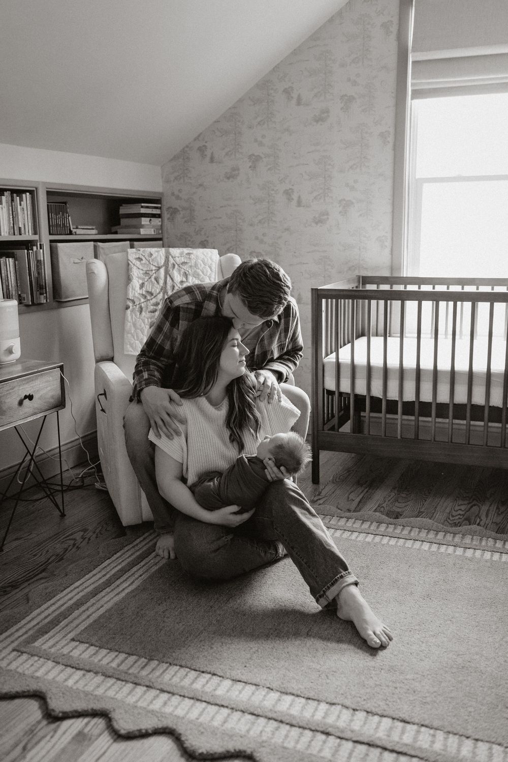 Black and white intimate family portrait in modern nursery with natural window light.