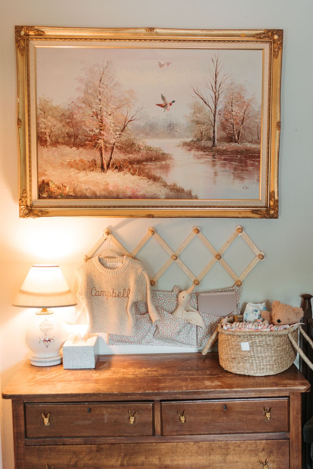 Rustic nursery decor with a framed landscape painting, wooden dresser and decorative accessories.