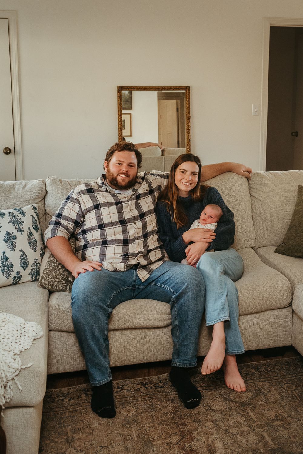 A relaxed family scene on a grey couch with a newborn baby in a comfortable home setting.