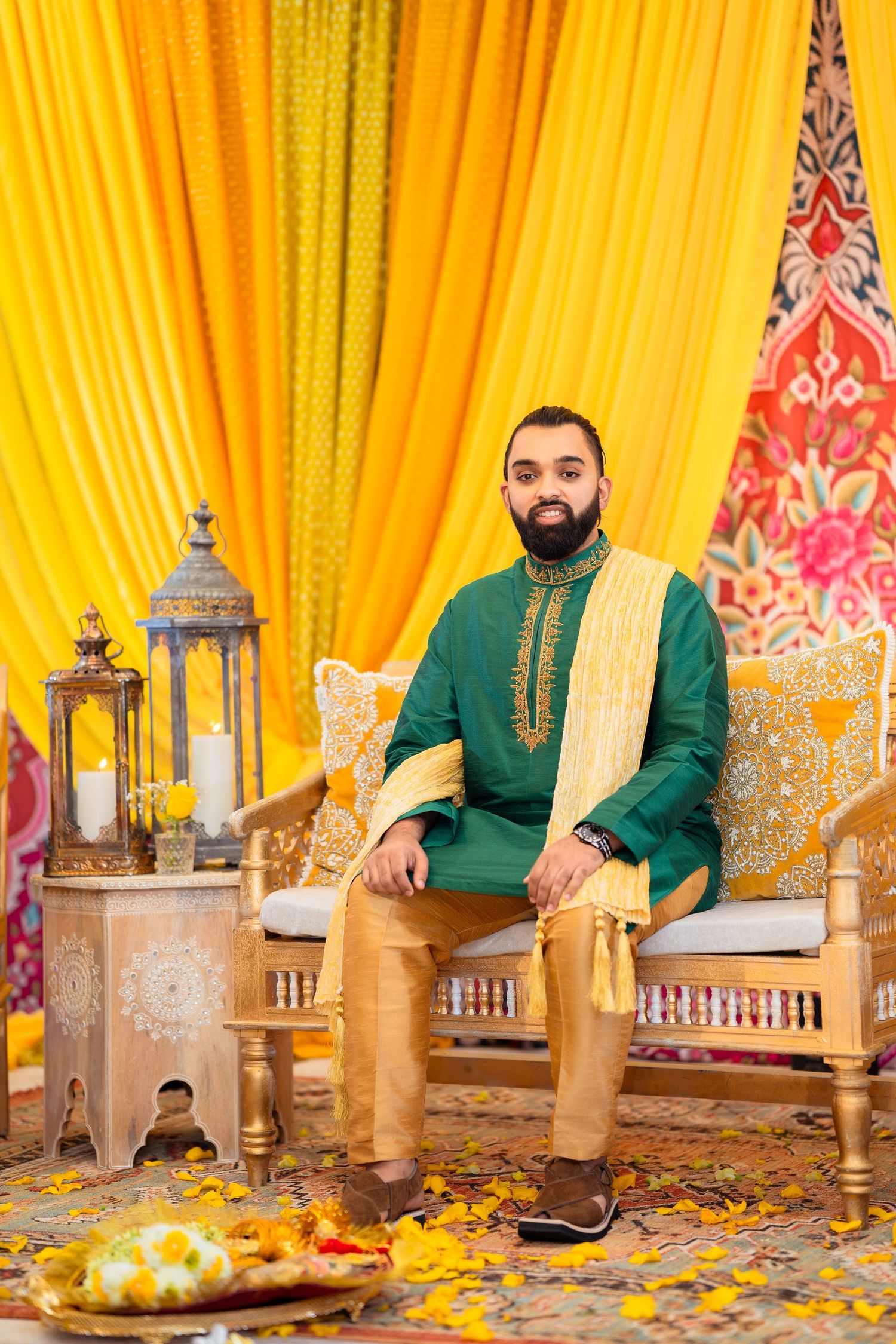 Traditional South Asian groom in green kurta sits on ornate golden chair against yellow backdrop with decorative lanterns.