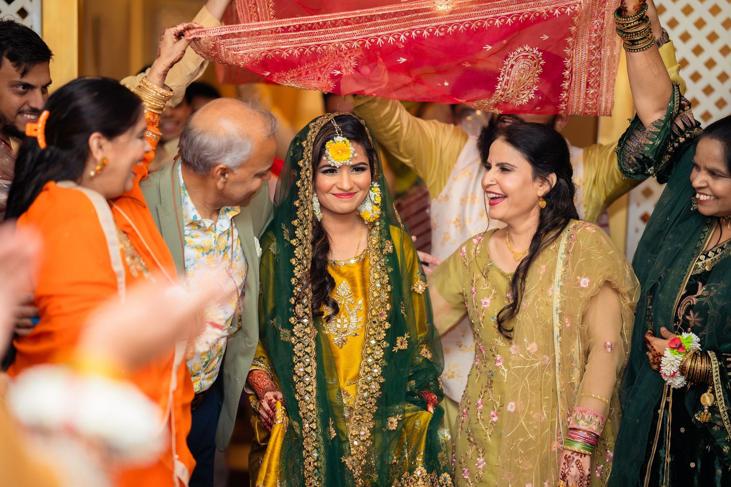 Celebratory moment during South Asian wedding ceremony with guests holding red dupatta over the bride.