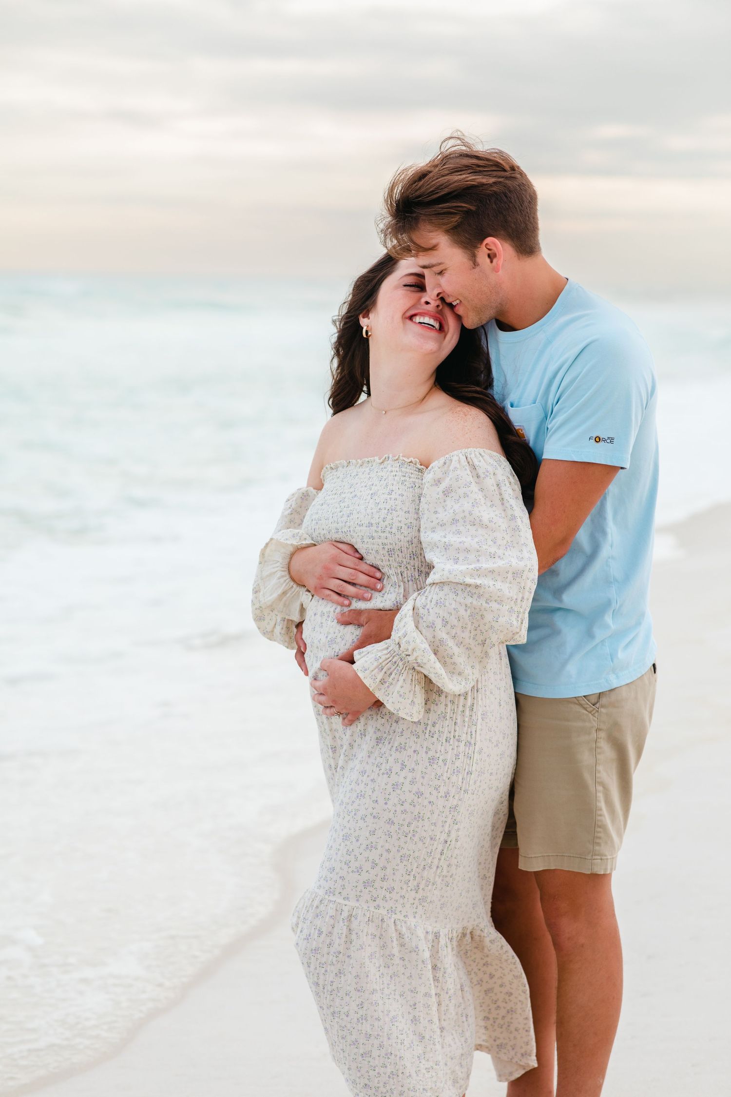A tender maternity moment shared between a couple on a white sandy beach.
