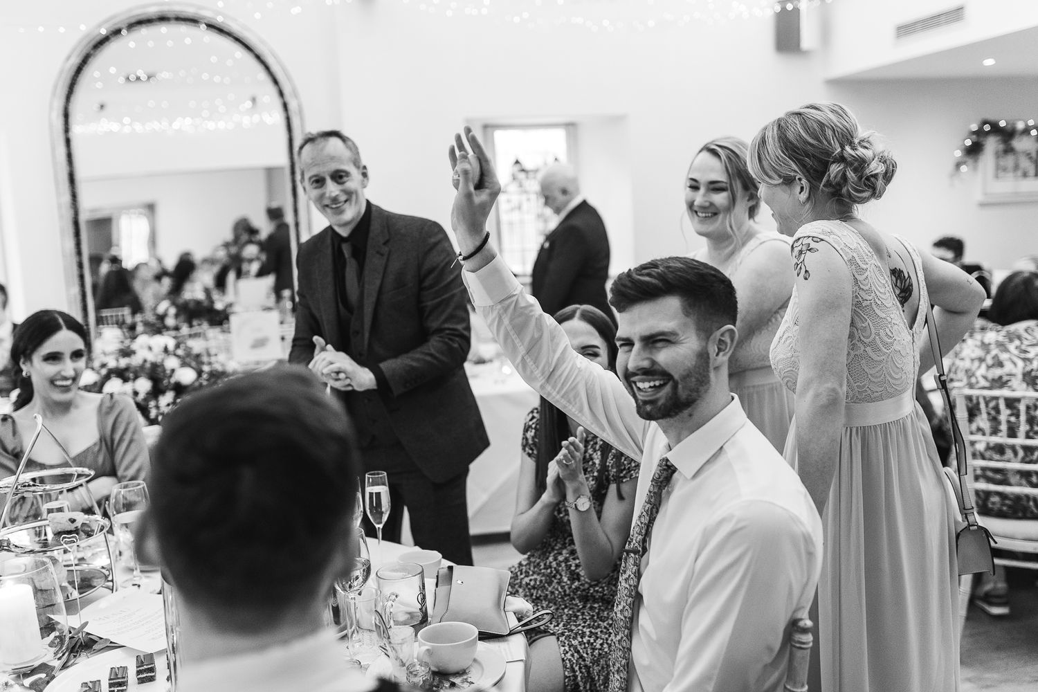 Black and white photo shows celebratory reactions during wedding reception festivities.