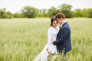 Bride and groom embracing in a lush green field on their wedding day.