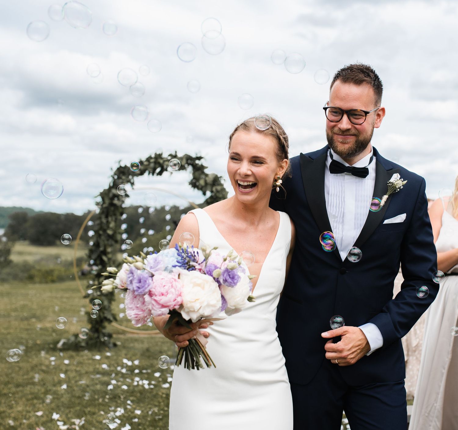 Happy newlyweds walk down the aisle amid flying confetti under a floral arch.