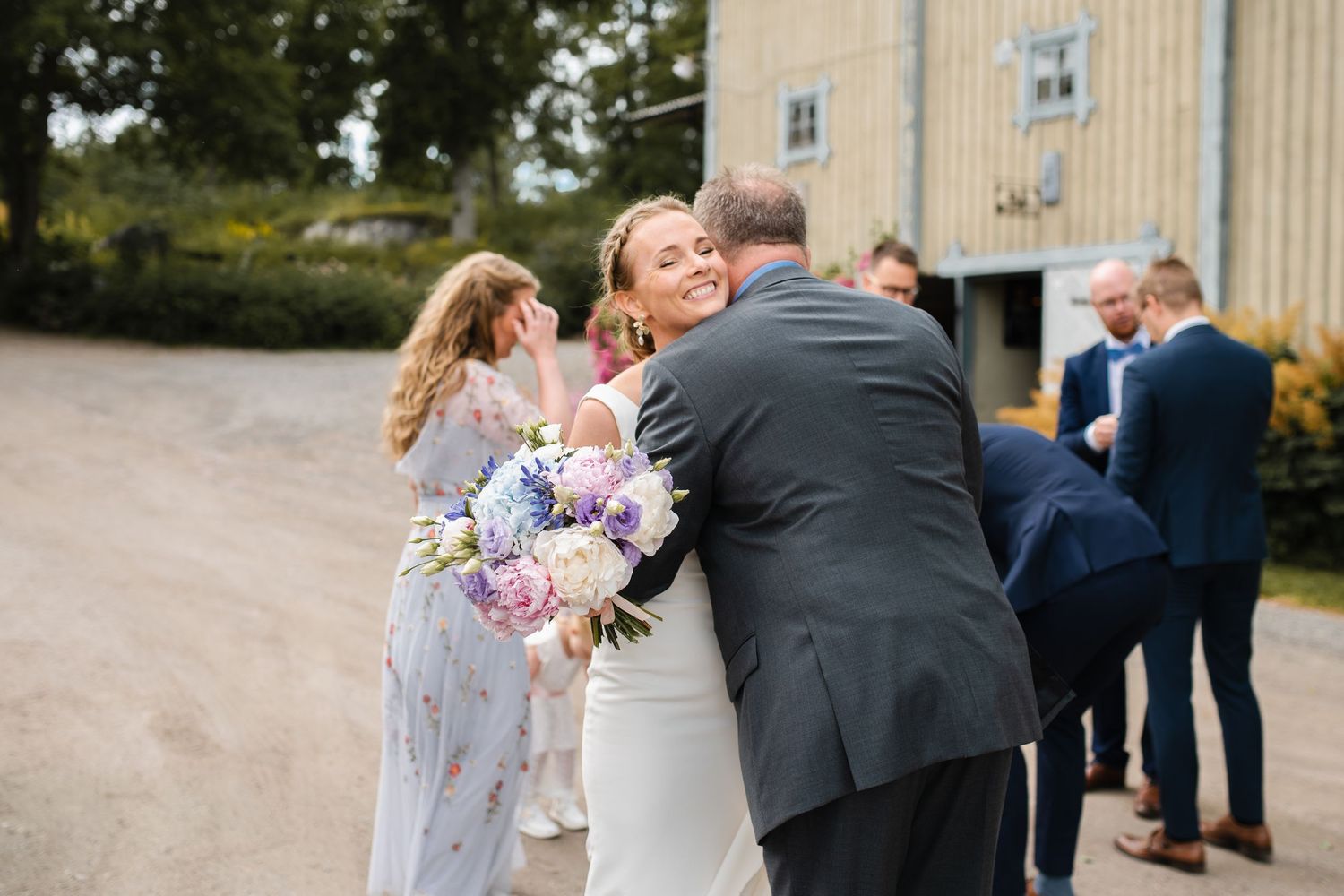 Emotional wedding celebration moment captured with bouquet and formal attire outside rustic building.