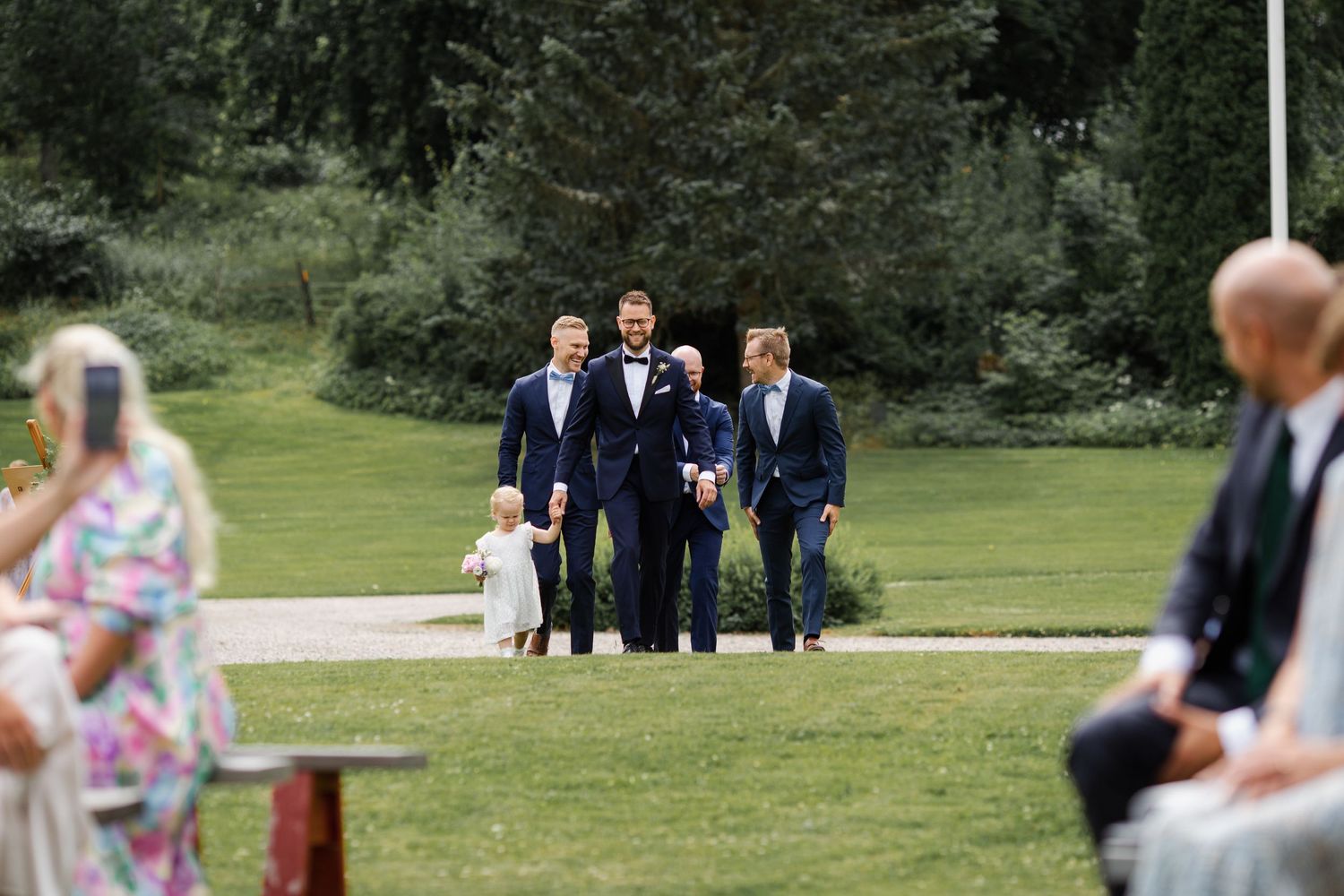 Wedding party members walking across lawn during outdoor ceremony.