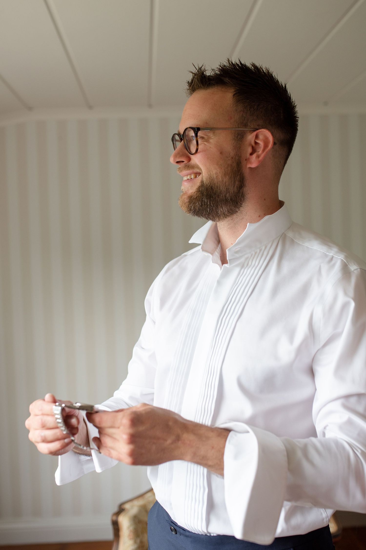 A smiling person in a formal white pleated shirt adjusting their cuffs.