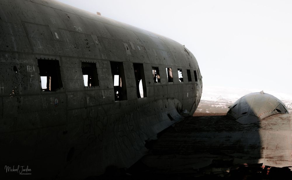 Abandoned aircraft fuselage with row of empty windows in desert landscape.