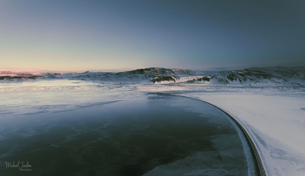 Curved snowy road winding through winter landscape at dusk.
