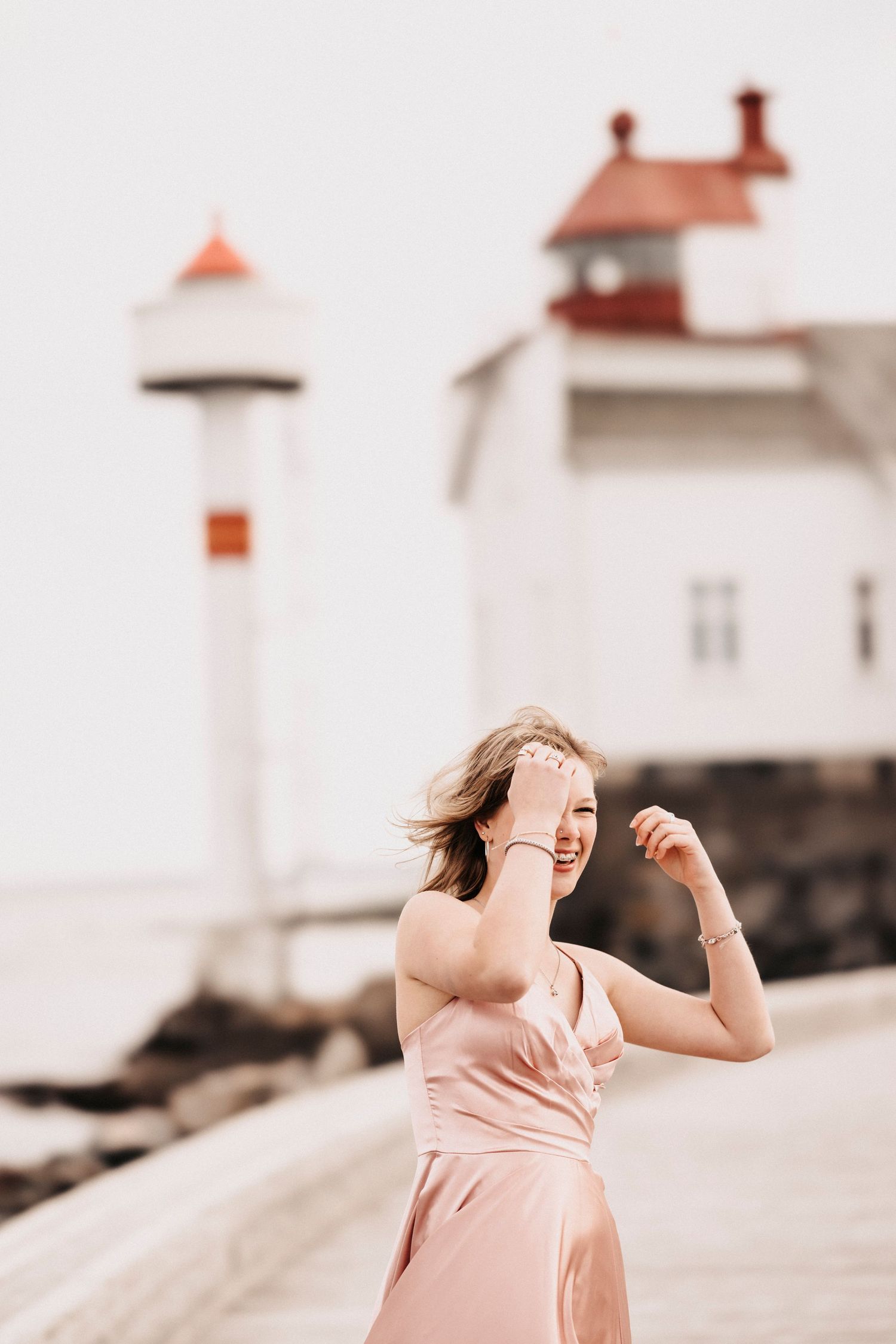 A dreamy portrait captured near a lighthouse with a flowing pink dress and windswept hair.