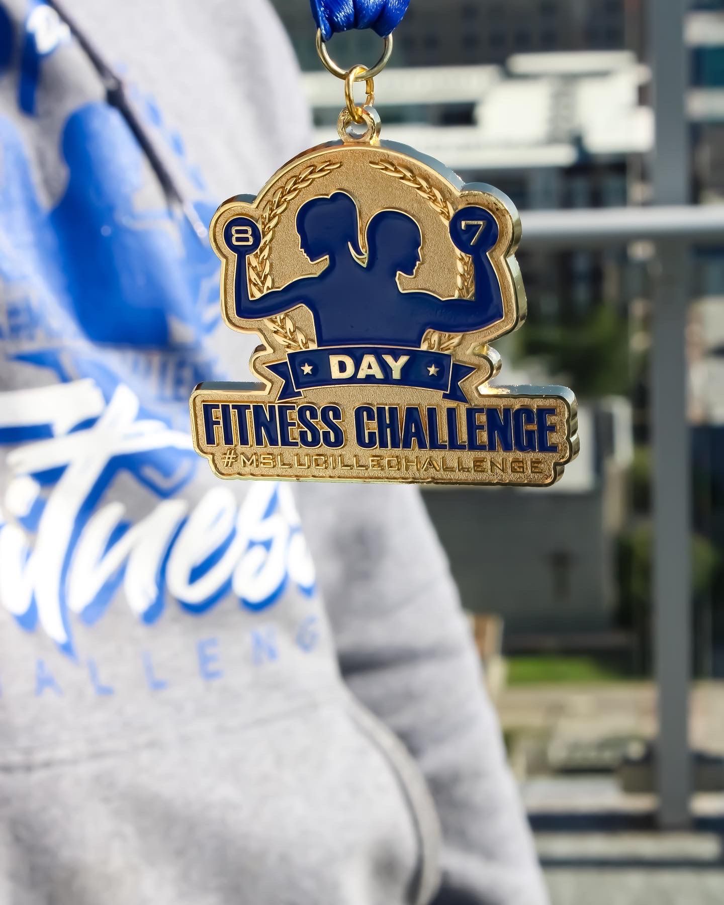 A gold fitness challenge medal with a silhouette design displayed against a gray sweatshirt.