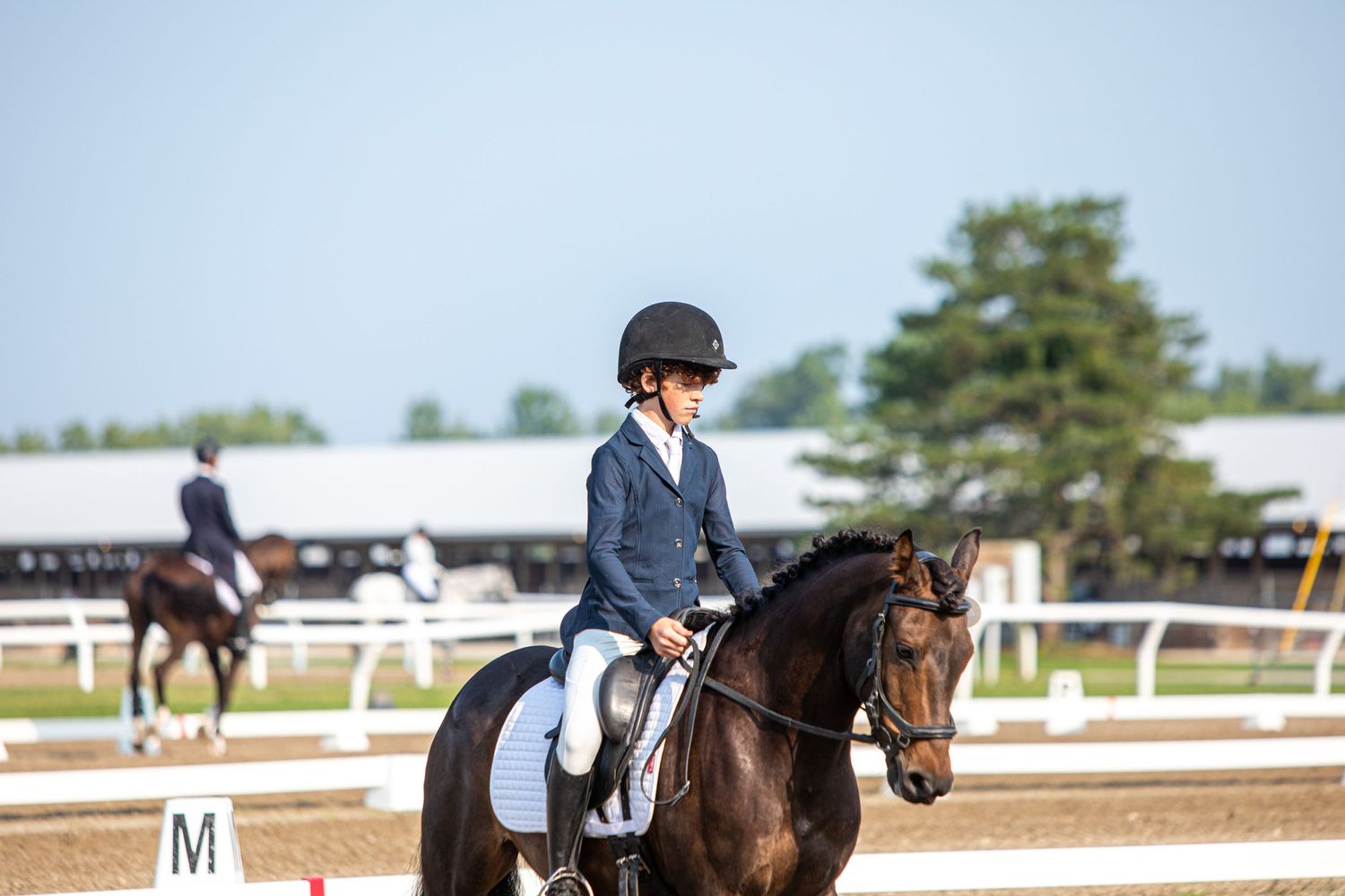 Dressage riders practicing in outdoor arena with white fence markers.