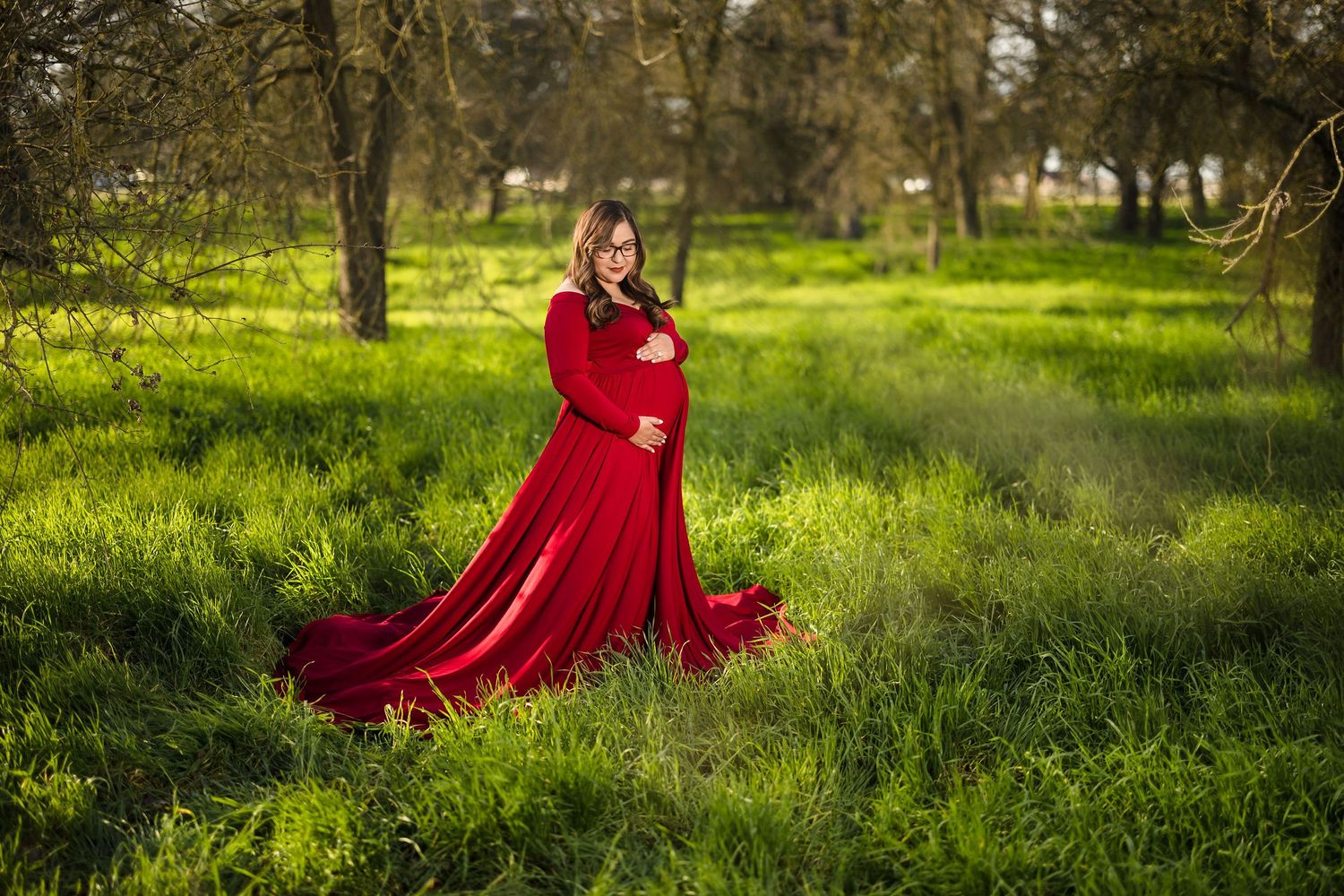 Person wearing a dramatic red gown poses in a lush green spring meadow.