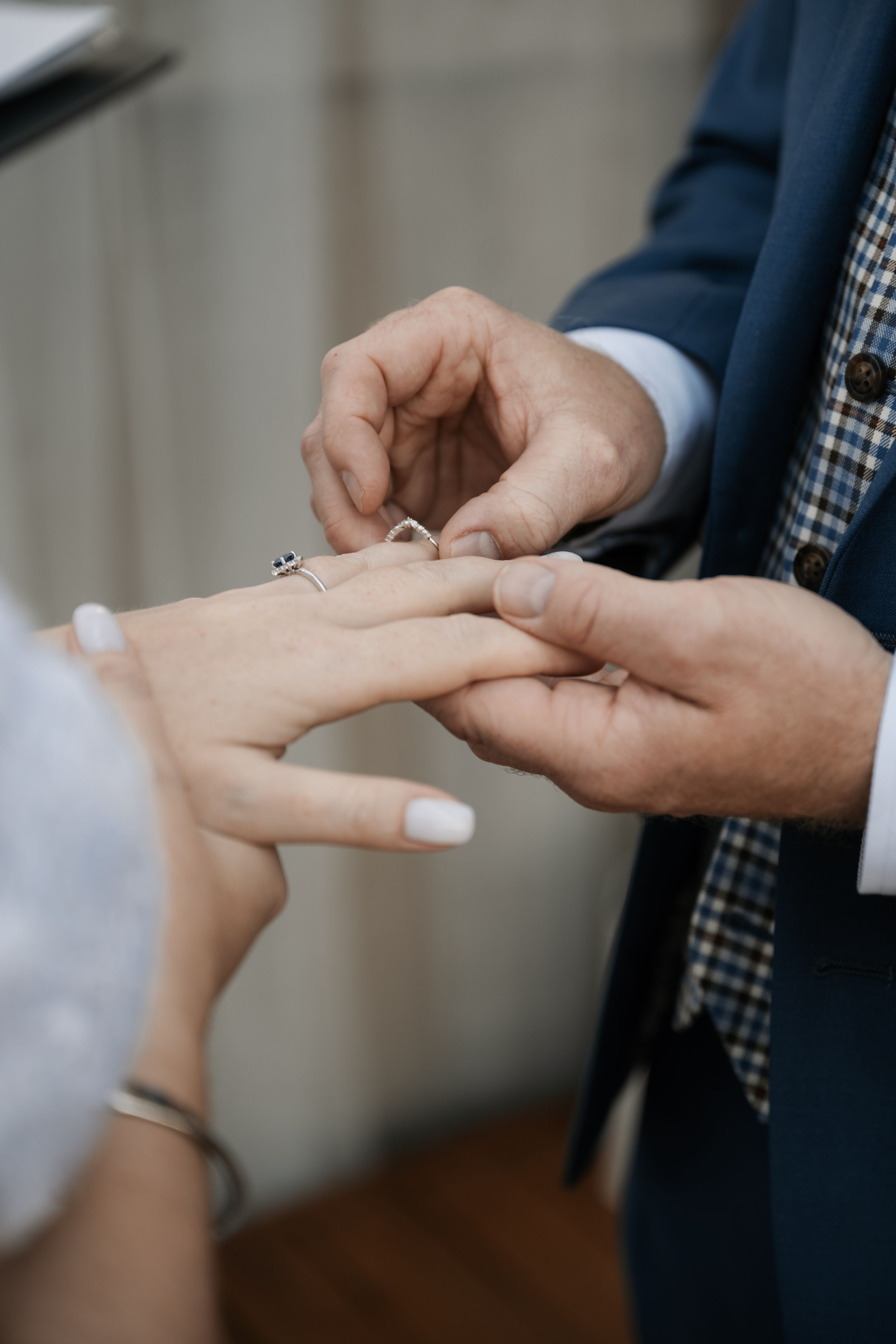 Close-up of hands exchanging a wedding ring during marriage ceremony with white nail polish visible.