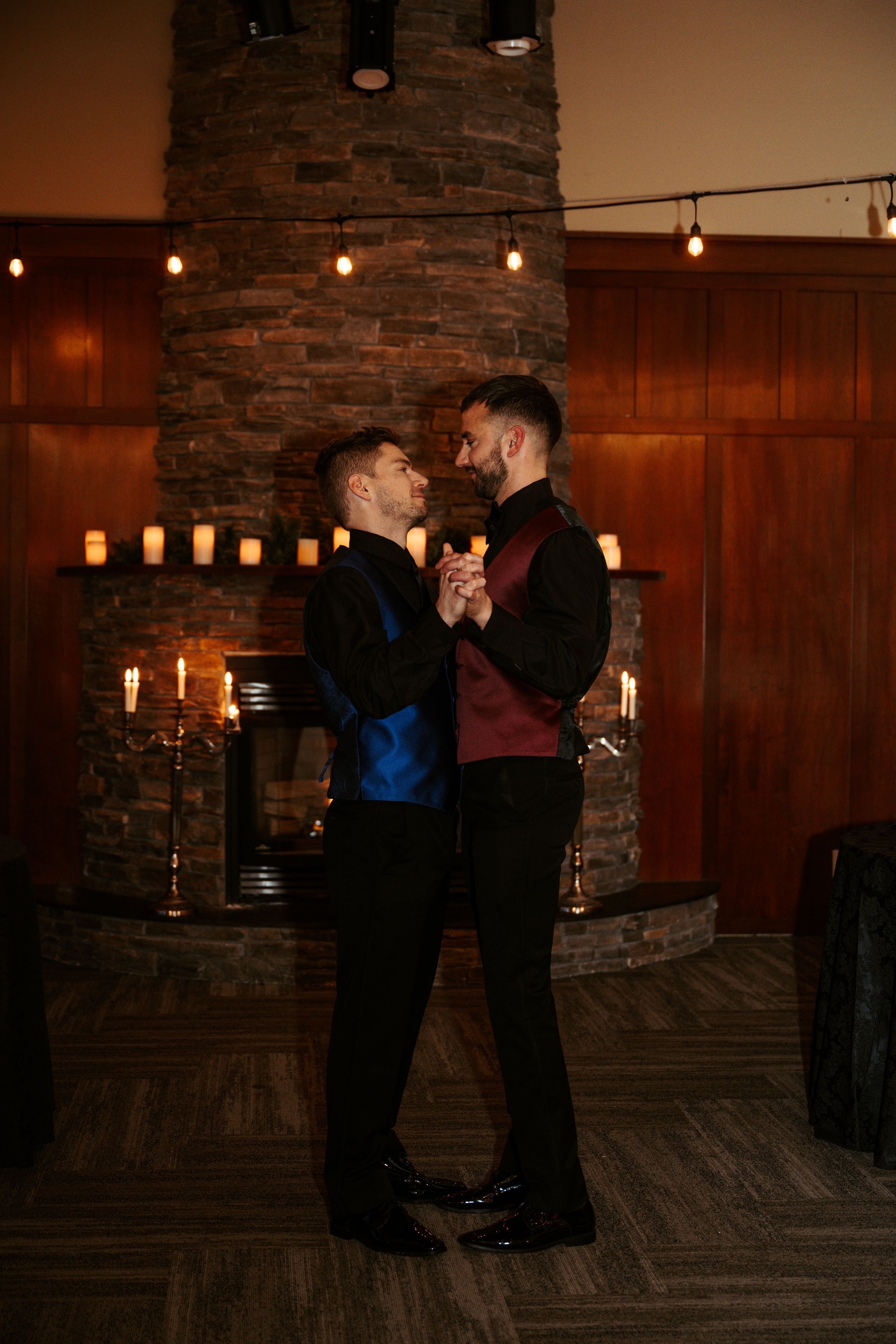 A romantic couple shares a dance moment in dim lighting with candles and string lights creating an intimate atmosphere.