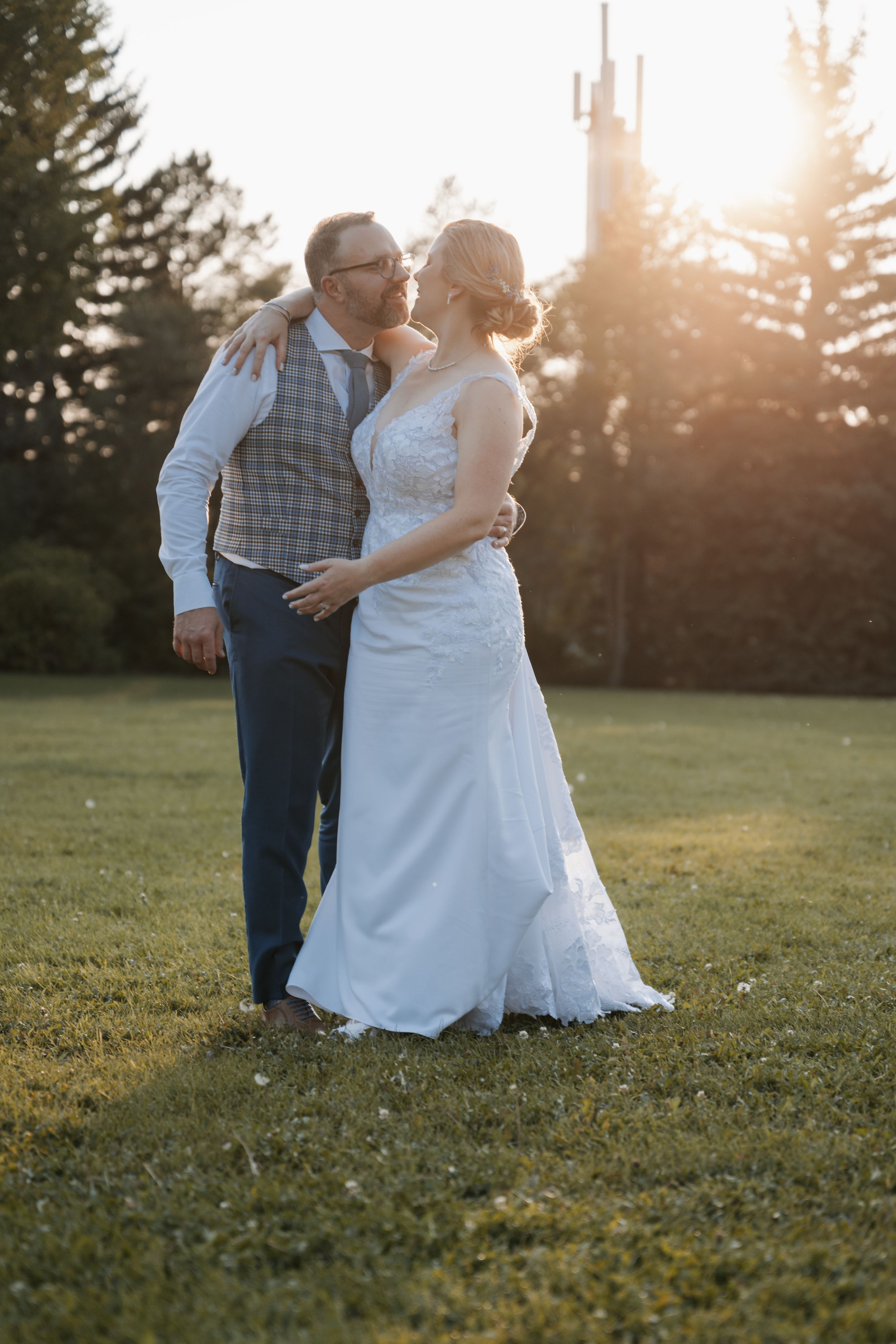 A couple embraces during golden hour sunset with a church steeple visible in the background.