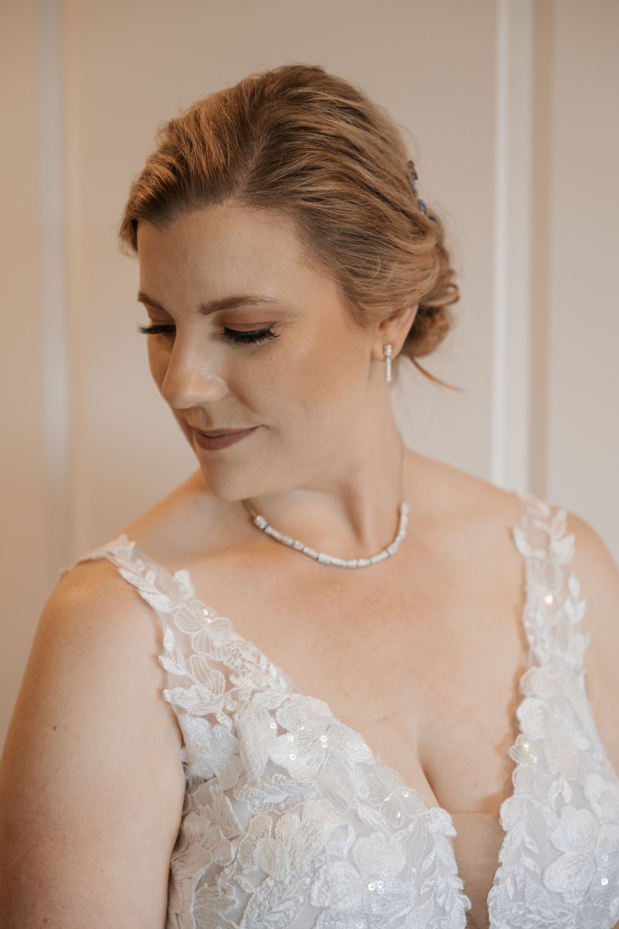 Elegant bridal portrait featuring delicate lace wedding dress, pearl necklace and soft romantic makeup in warm lighting.