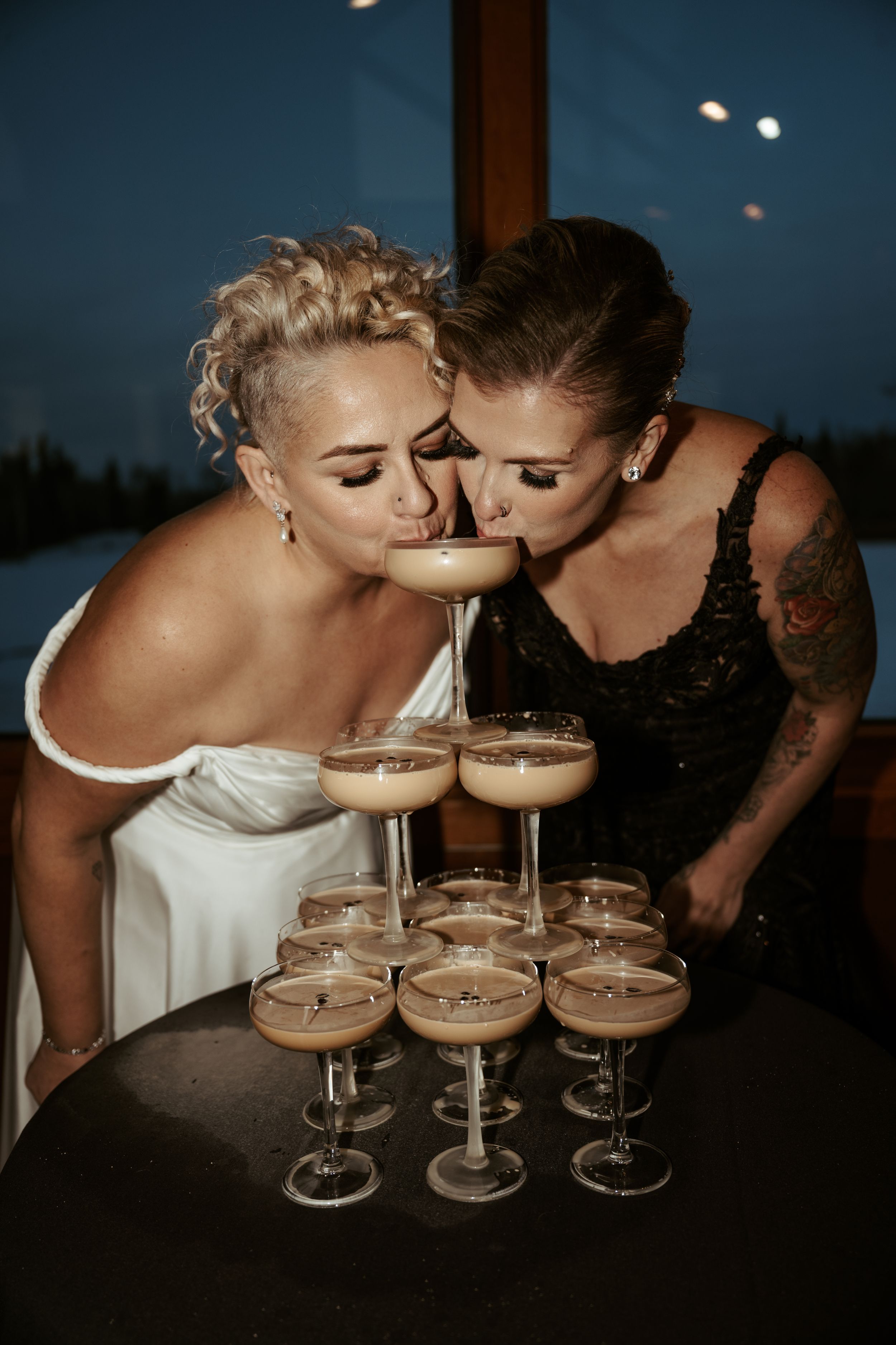 Two people in formal attire lean close together over a display of coupe cocktail glasses filled with espresso martinis.