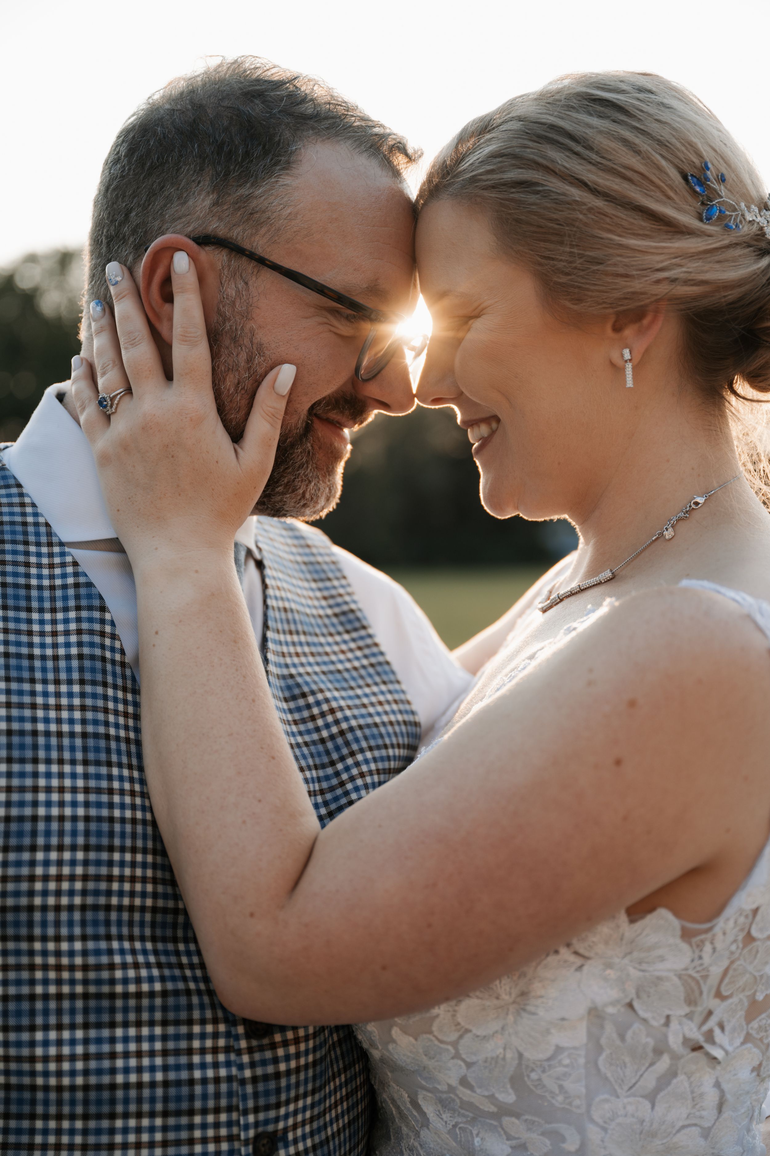 A tender moment between newlyweds with sunlight peeking between them as they share an intimate embrace outdoors.