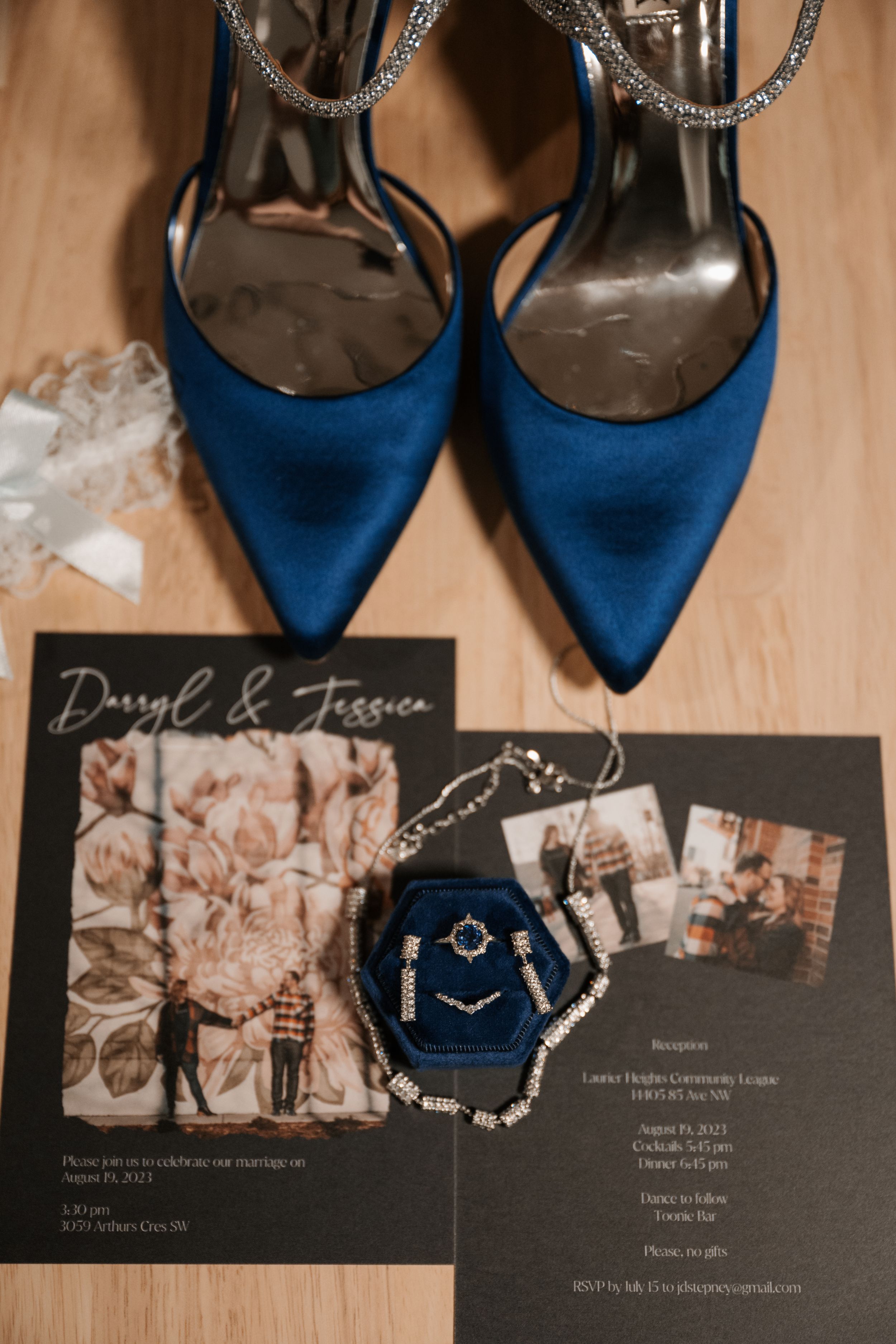 Blue satin heels and a wedding invitation with photos displayed on a wooden surface create an elegant bridal detail shot.