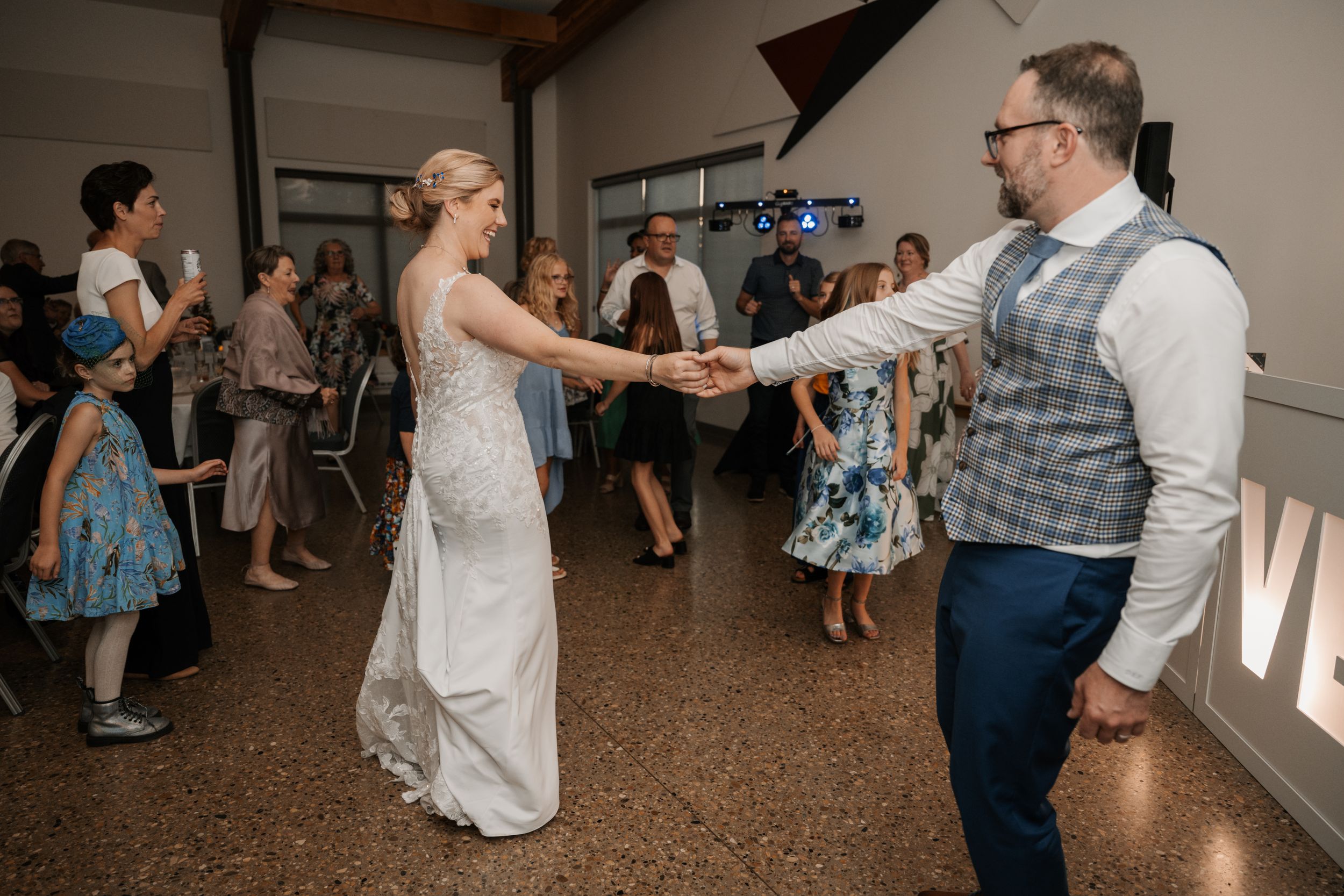Wedding guests dancing together at a reception on a dance floor with illuminated decor in the background.