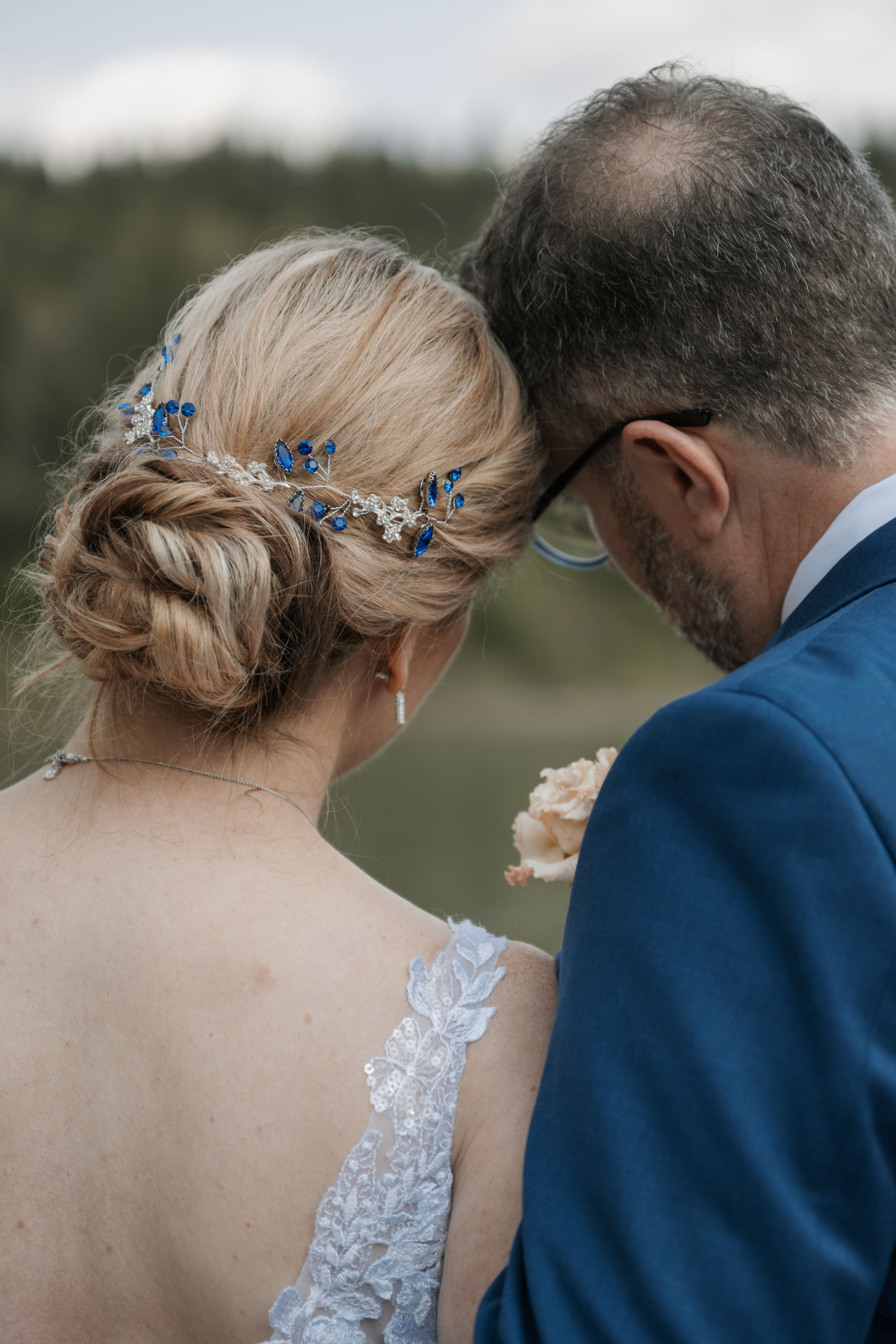 Bride wearing delicate blue hair accessories and lace dress stands beside groom in navy suit during outdoor ceremony.