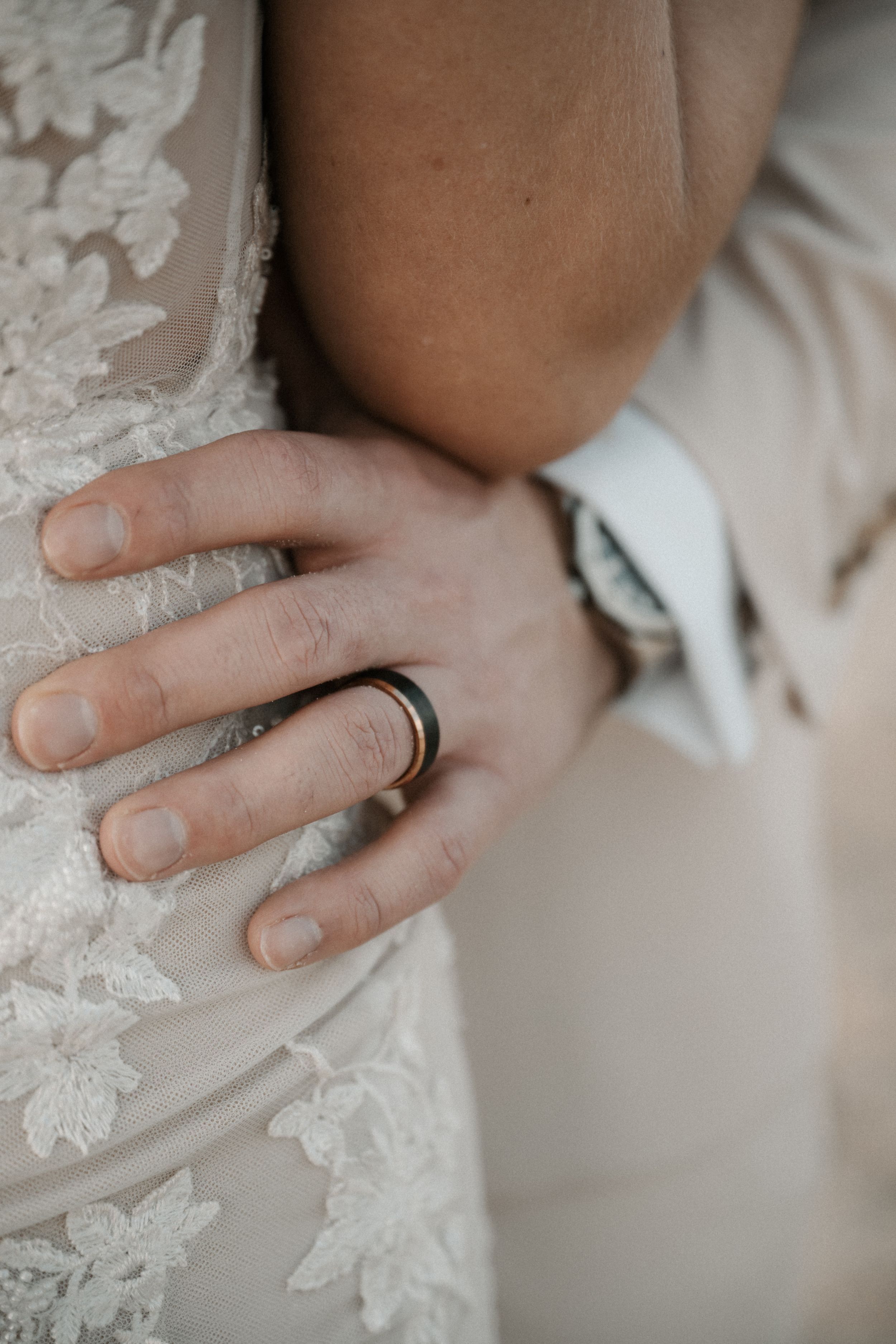 Close-up of hands with wedding rings touching lace wedding dress fabric in intimate romantic moment.