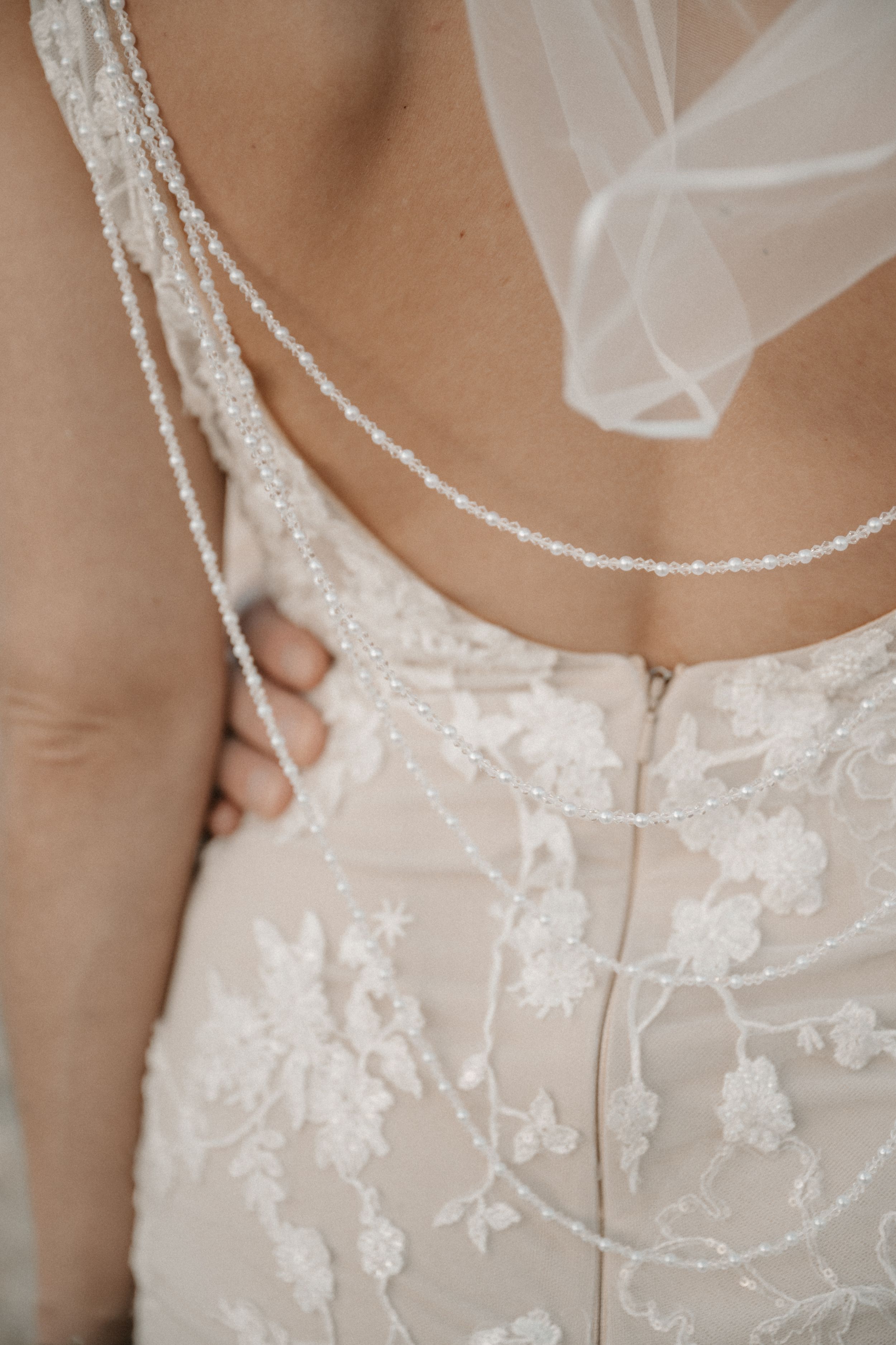 Close-up detail of delicate lace and beading on a white wedding dress with sheer tulle veil and floral embroidery.