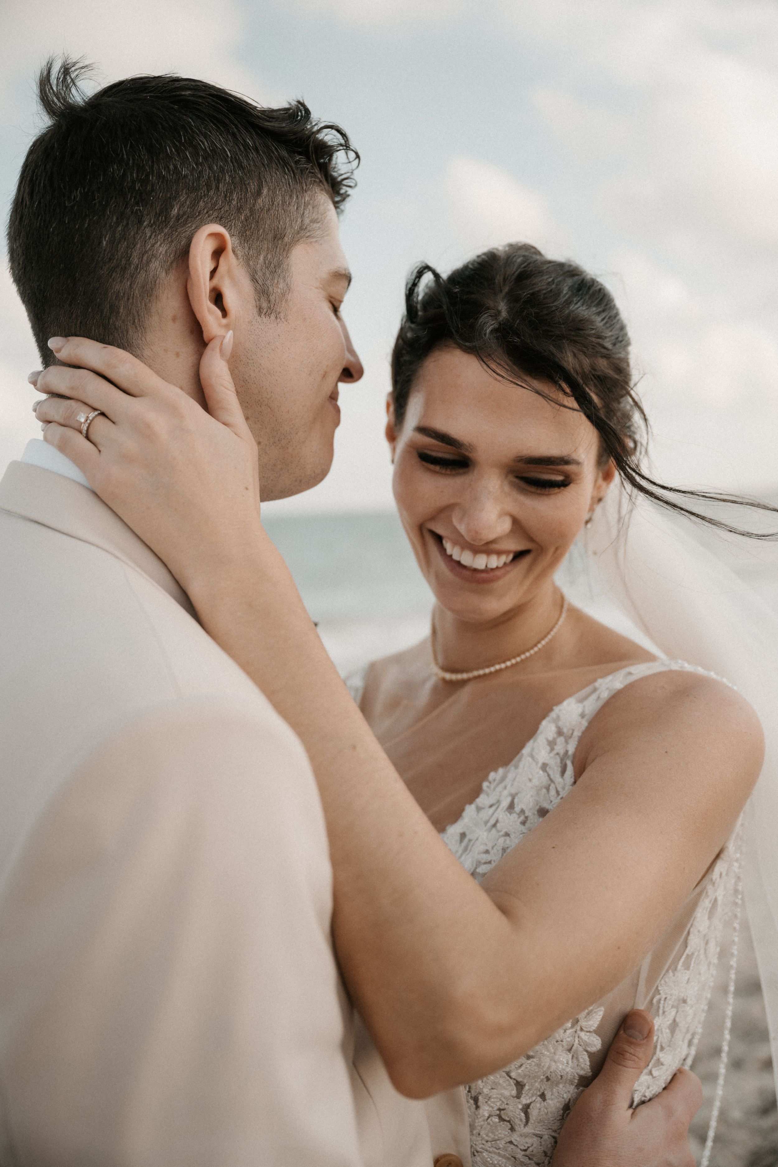A romantic beach wedding moment showing a tender embrace between newlyweds against a cloudy sky backdrop.