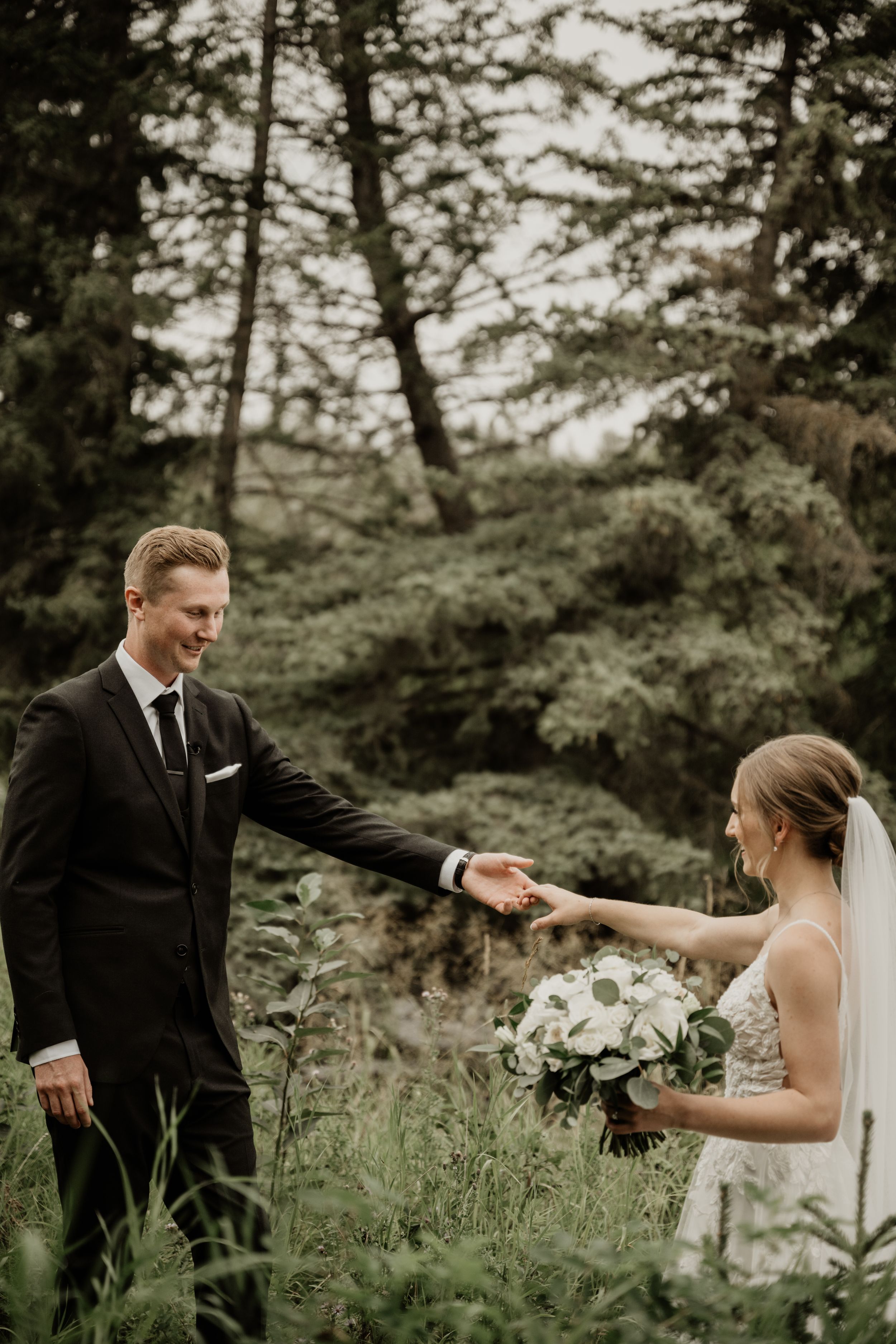 A couple shares an intimate moment in the woods during their wedding photoshoot, surrounded by lush greenery.