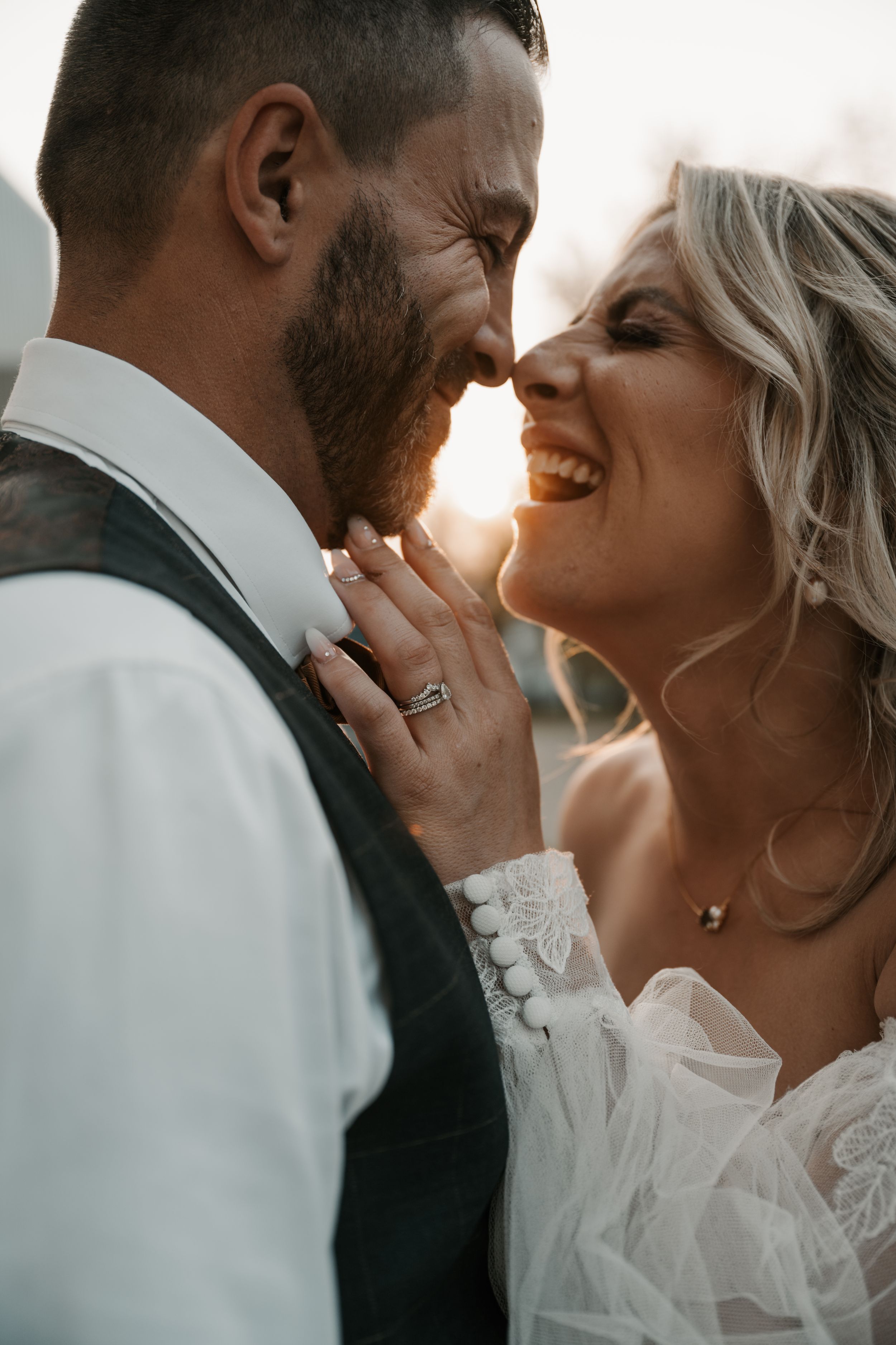 Romantic wedding couple shares intimate moment of laughter while embracing during golden hour sunset.