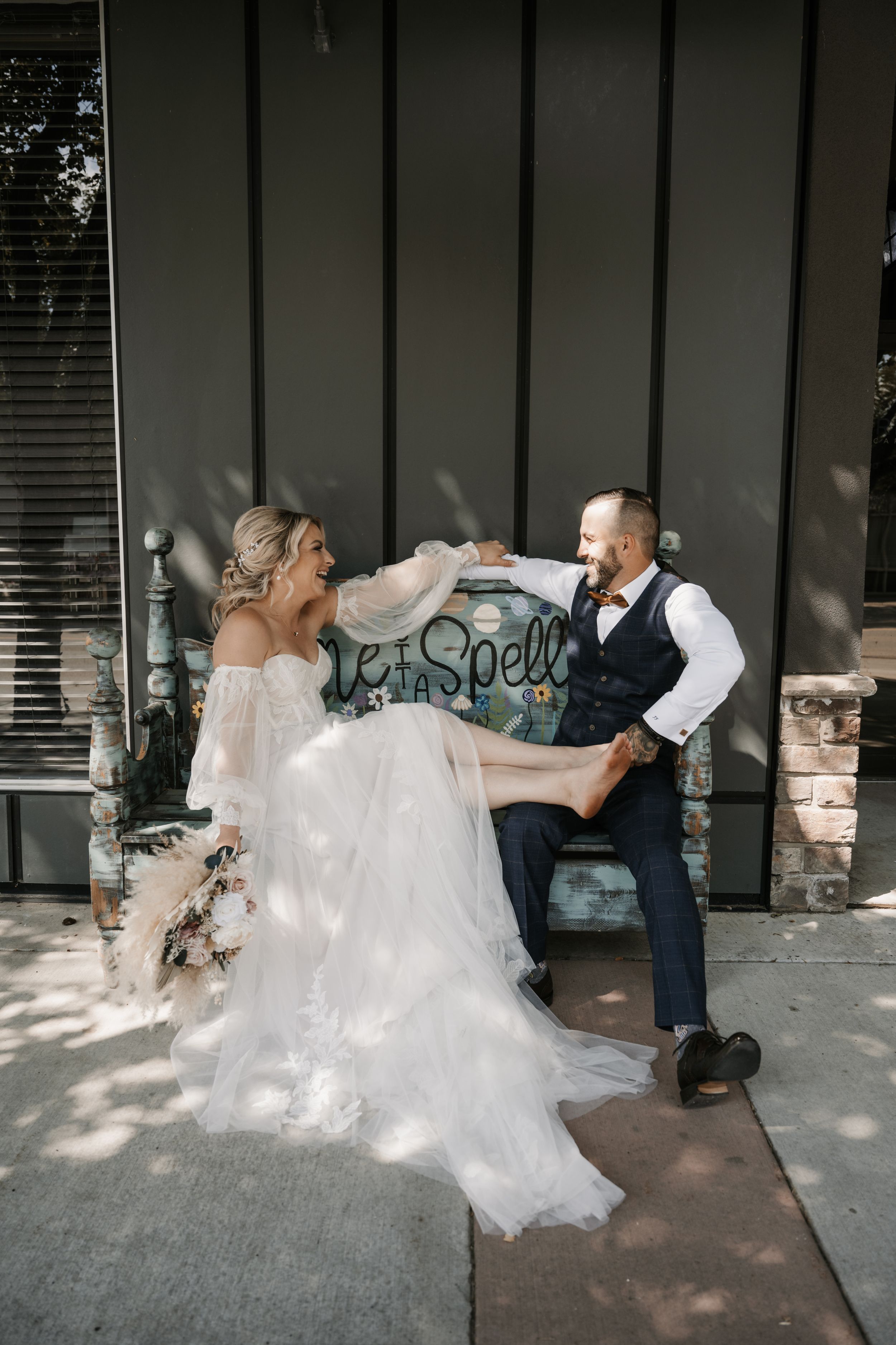 A couple shares a playful moment in front of a storefront sign on their wedding day.