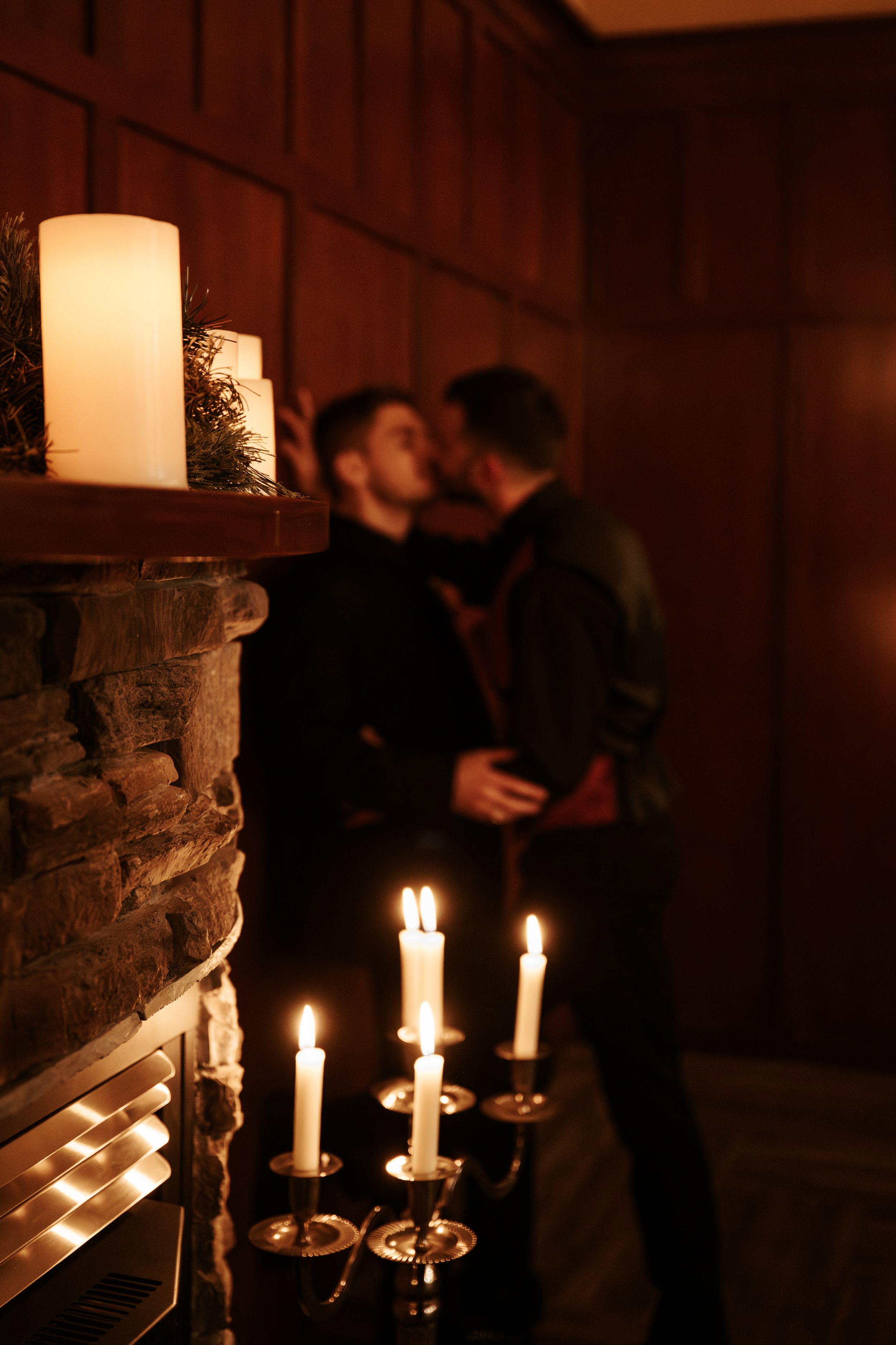 Lit candles on a candlestick holder create romantic ambient lighting in a dimly lit room with stone and wooden walls.