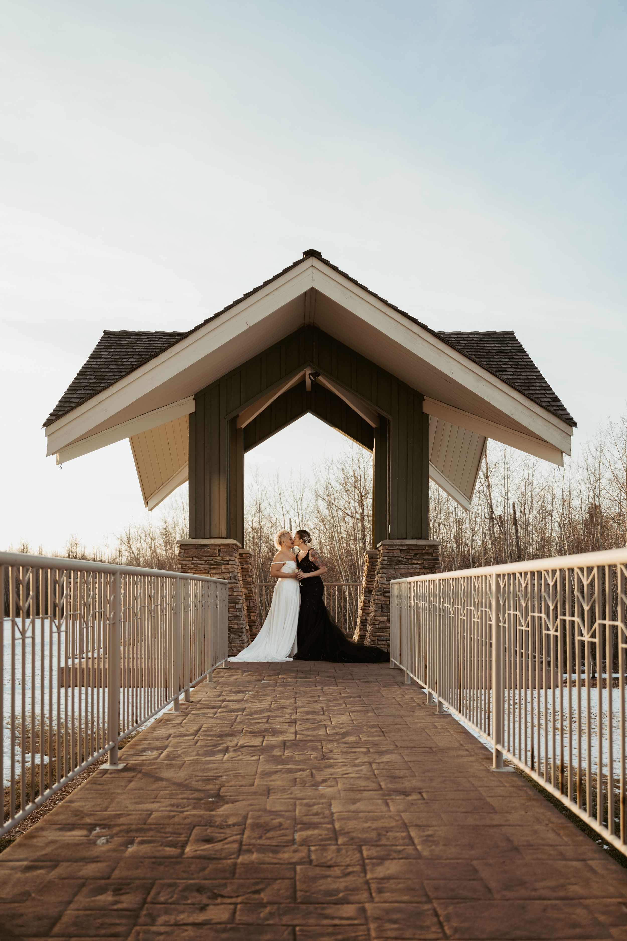 A couple sharing a romantic moment under a covered wooden bridge walkway during a winter wedding photoshoot.
