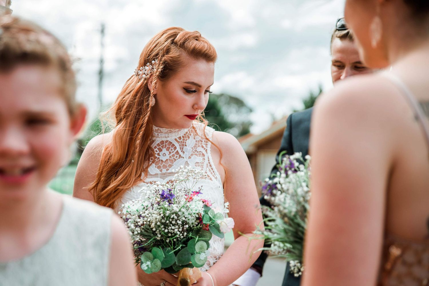 White lace wedding dress with delicate braided hairstyle and baby's breath bouquet at outdoor ceremony.