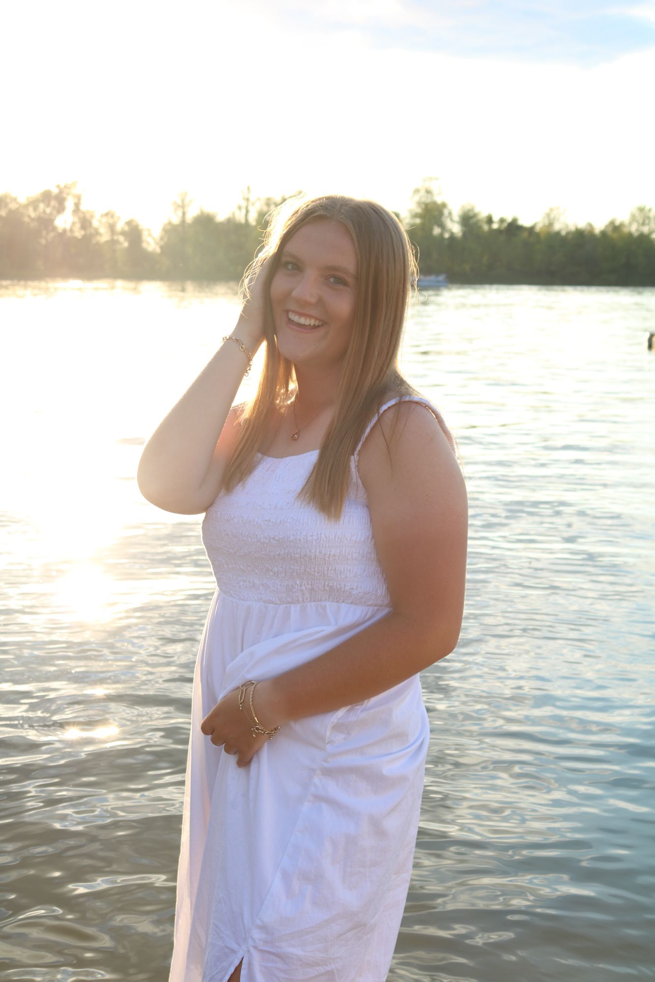 A glowing sunset portrait of someone in a white dress by a serene lake.