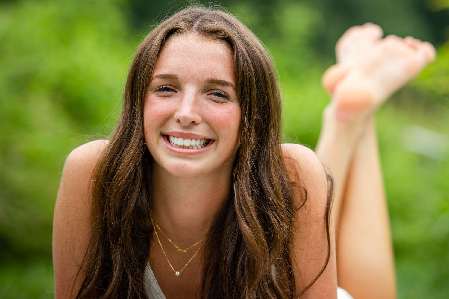 Portrait of someone laying on grass with brown hair and a bright smile against a green background.