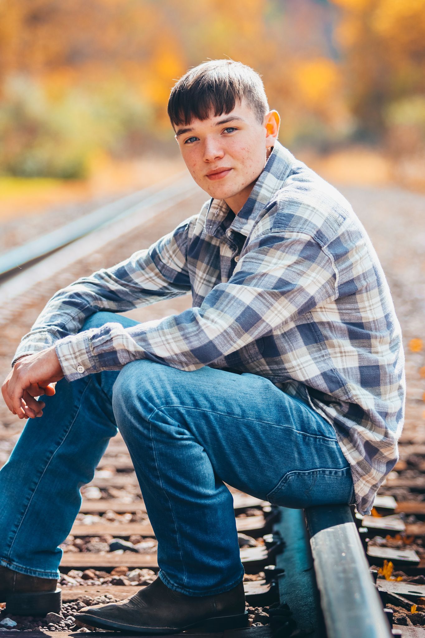 Casual portrait on railroad tracks wearing plaid shirt and jeans in fall scenery.