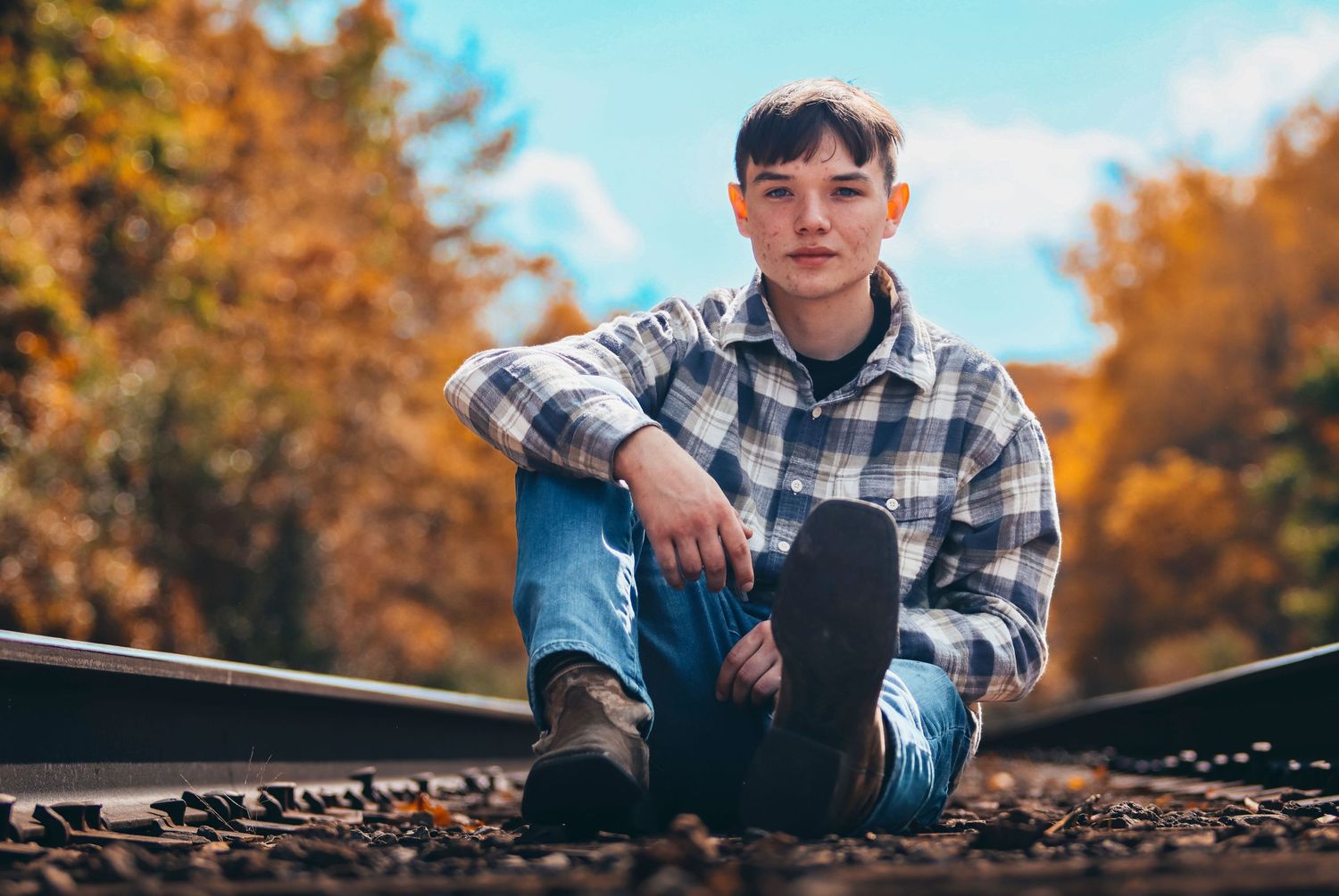 Portrait sitting on railroad tracks with autumn foliage in background.
